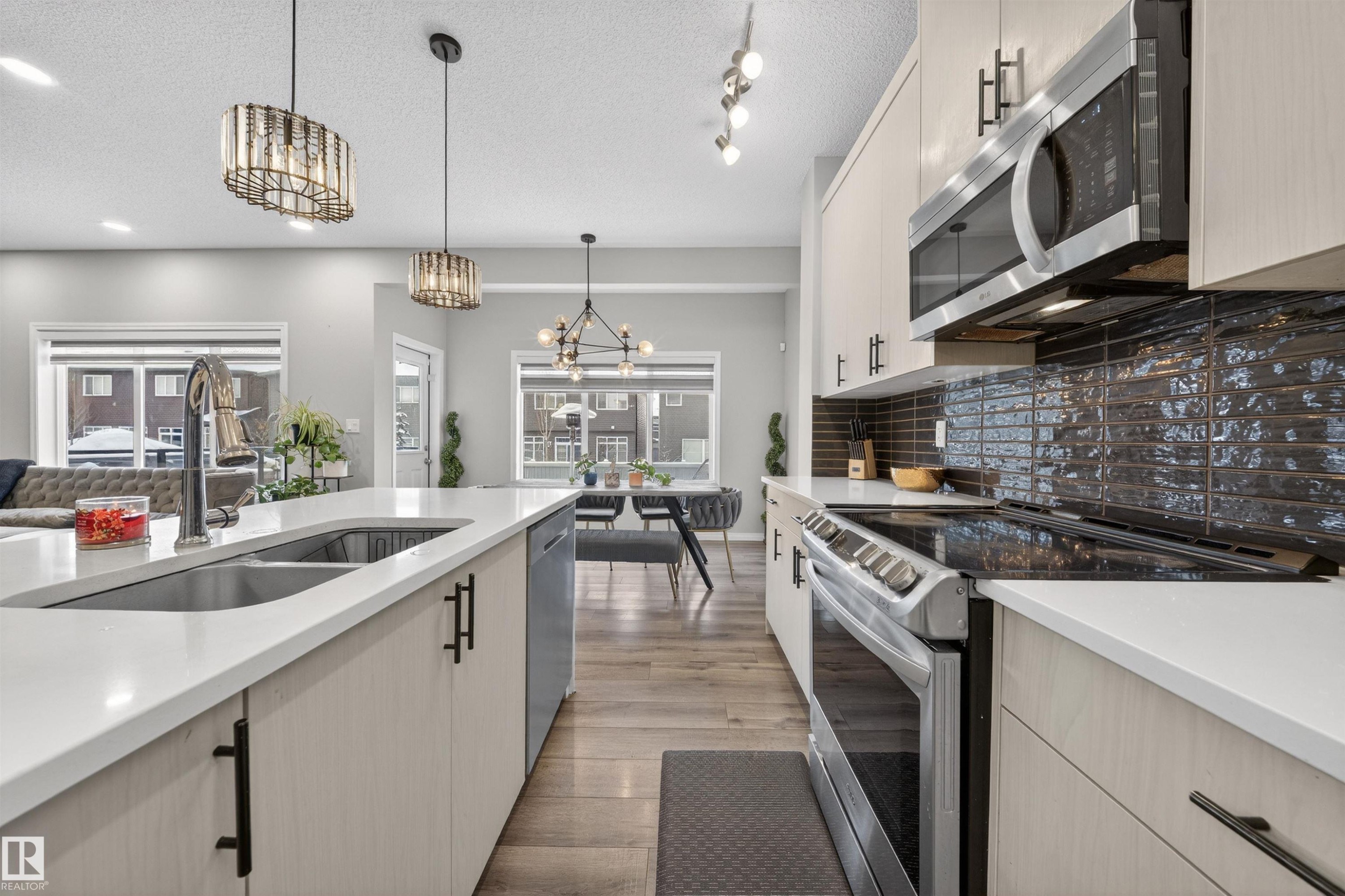Contemporary kitchen featuring a large island with an undermount sink, light-toned cabinetry with matte black hardware, stainless steel appliances, dark subway tile backsplash, and wood-finish flooring - 6085 King Landing, Edmonton, AB - Indoor Photo Showing Kitchen With Double Sink With Upgraded Kitchen
