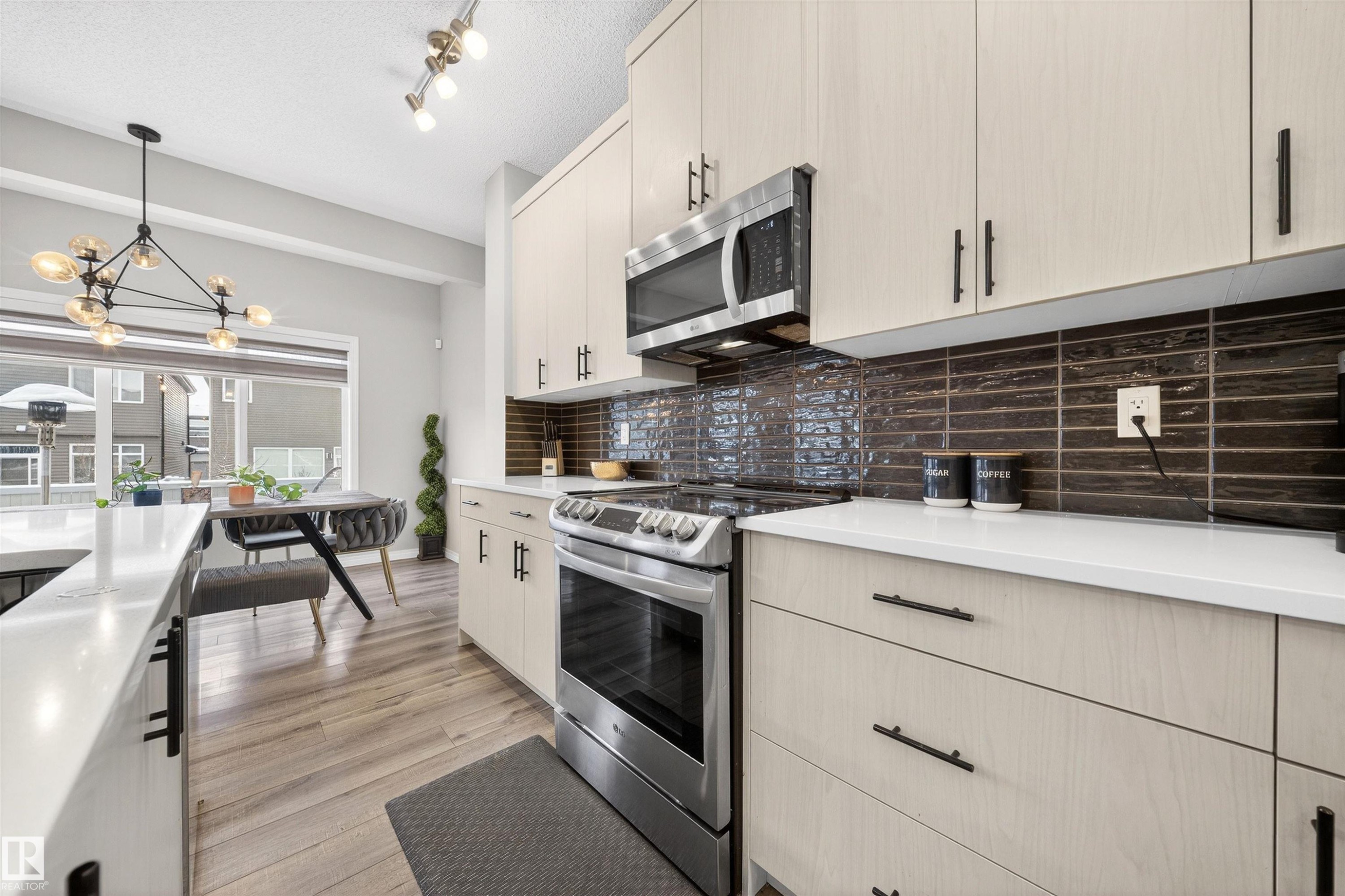 Modern kitchen featuring light-toned cabinetry, stainless steel appliances, a dark tile backsplash, white countertops, and wood-finish flooring - 6085 King Landing, Edmonton, AB - Indoor Photo Showing Kitchen With Upgraded Kitchen
