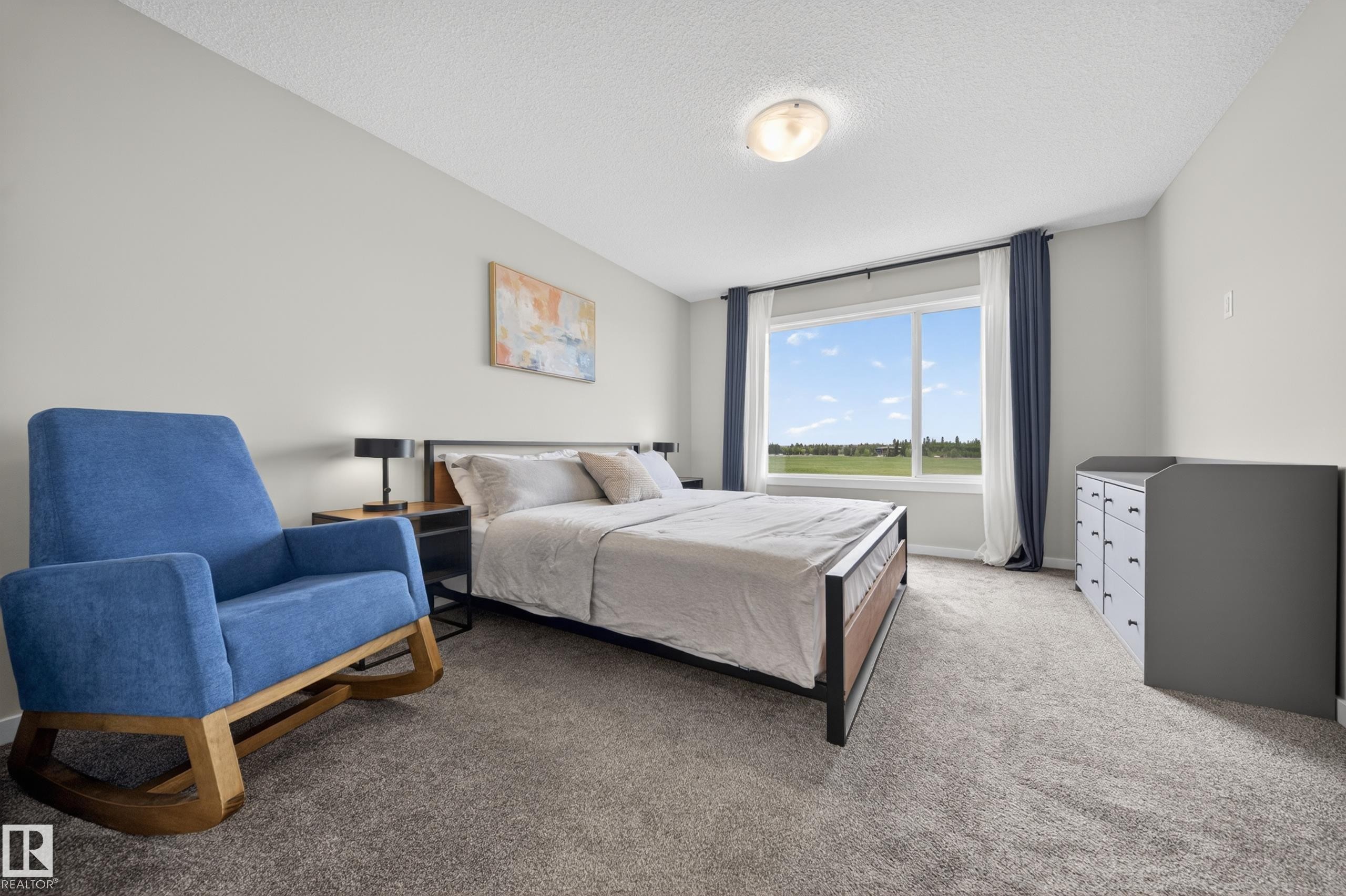 Spacious bedroom featuring light gray walls, plush gray carpeting, a large window with white trim, and a semi-flush mount ceiling light - 3337 Kulay Way, Edmonton, AB - Indoor Photo Showing Bedroom