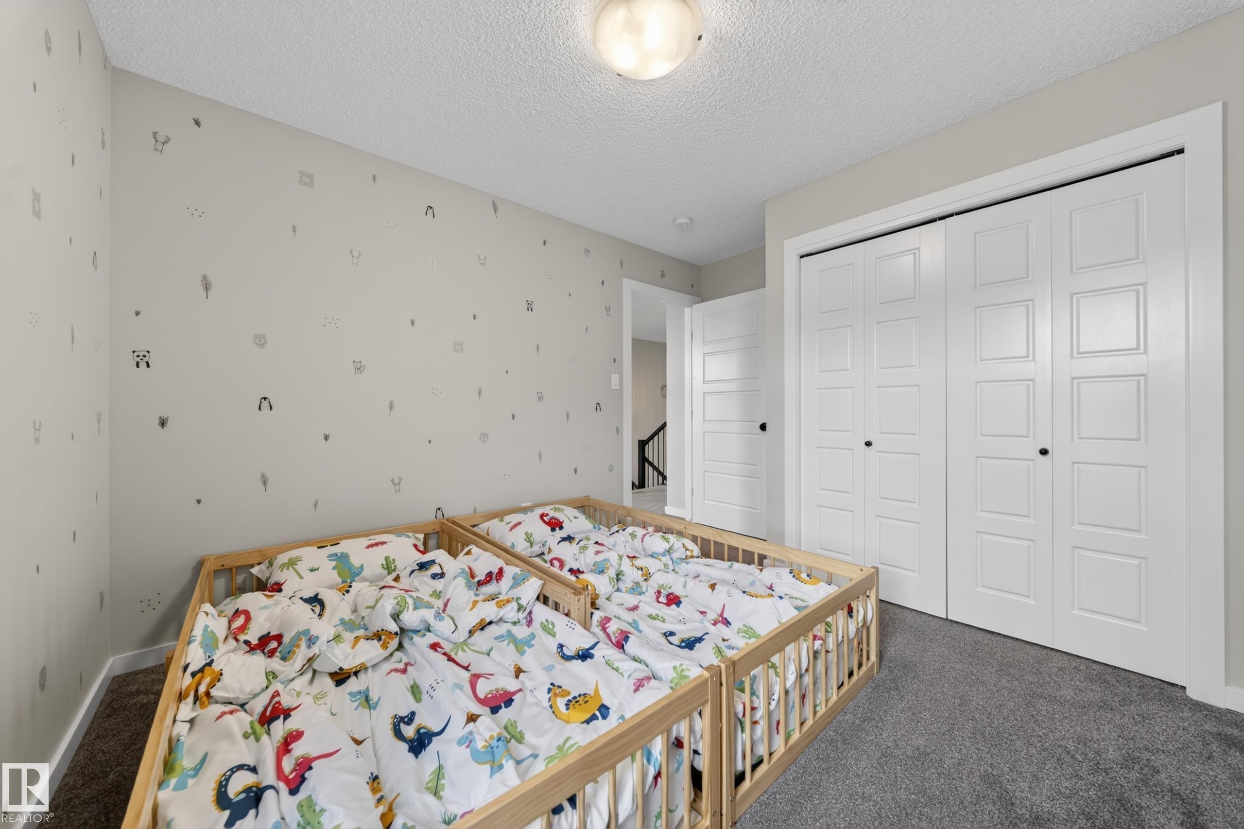 Carpeted room featuring a ceiling-mounted light fixture, light gray walls with decorative accents, and white paneled bi-fold closet doors with black hardware - 3337 Kulay Way, Edmonton, AB - Indoor Photo Showing Bedroom
