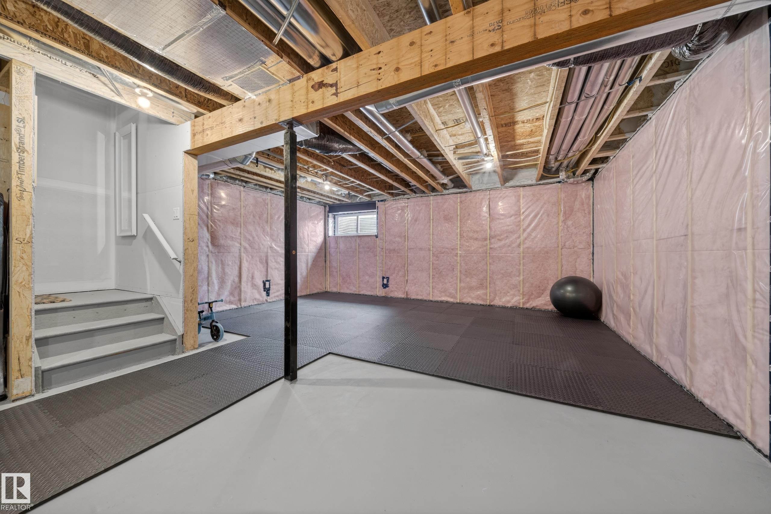 Spacious unfinished lower level featuring exposed wood joists and structural beams, a partial staircase with painted treads, and visible wall insulation - 3337 Kulay Way, Edmonton, AB - Indoor Photo Showing Basement