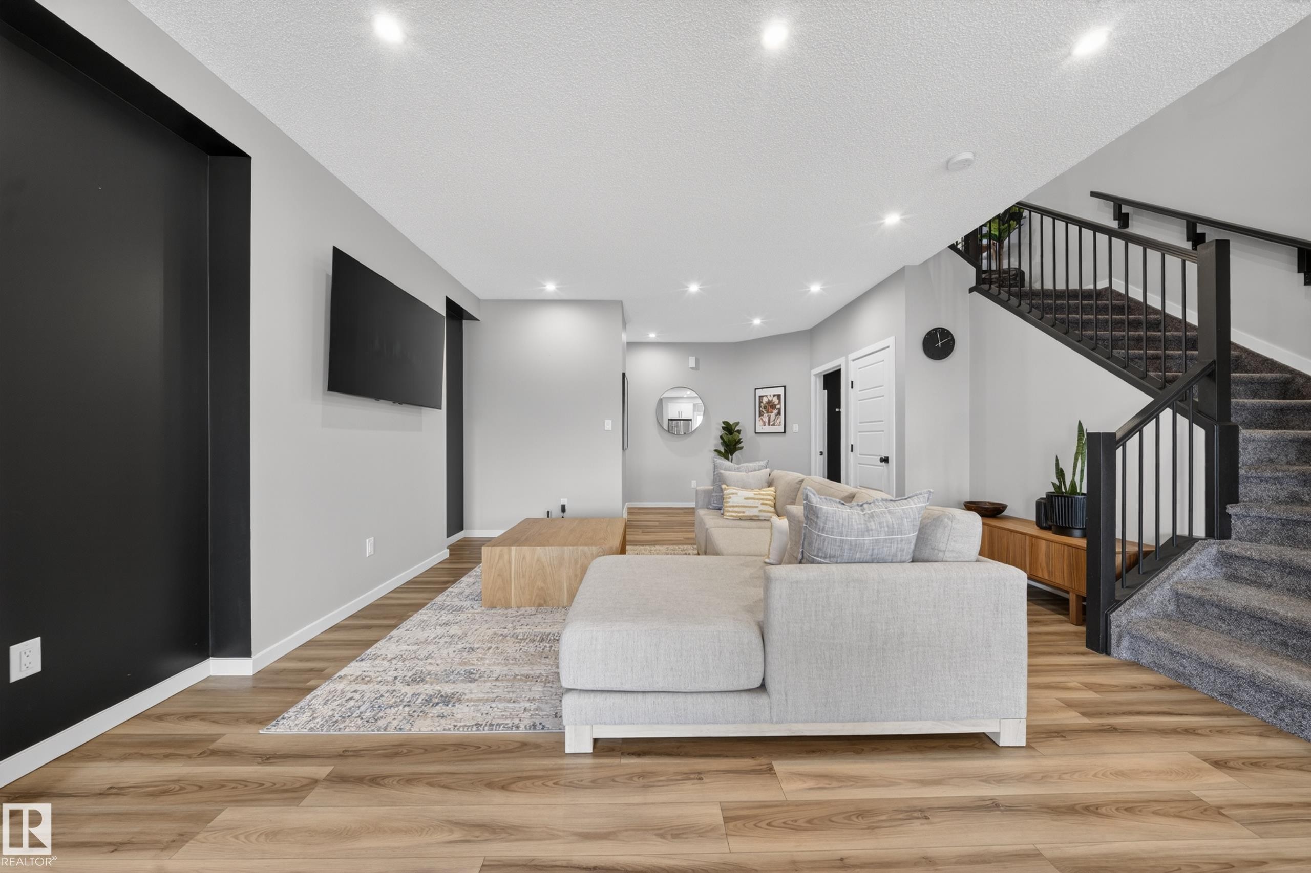 Spacious living area featuring wood-finish flooring, recessed lighting, and a modern staircase with black railings - 3337 Kulay Way, Edmonton, AB - Indoor