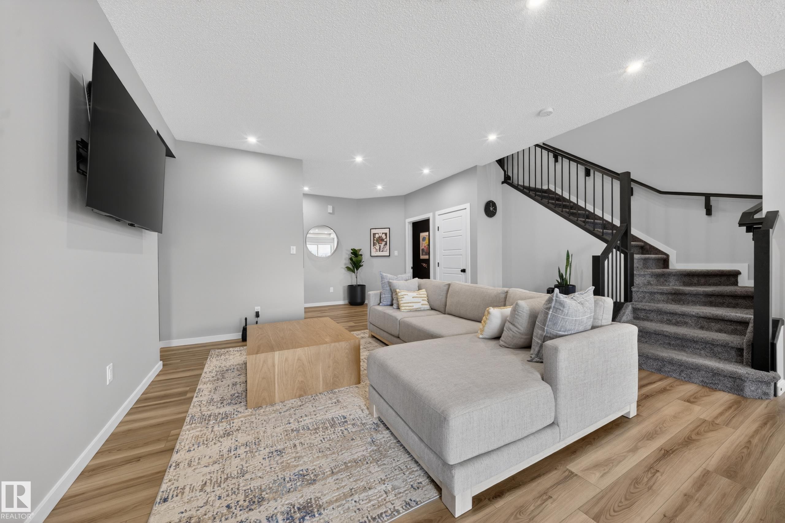 Spacious living area featuring wood-finish flooring, recessed lighting, and a contemporary staircase with black railings - 3337 Kulay Way, Edmonton, AB - Indoor