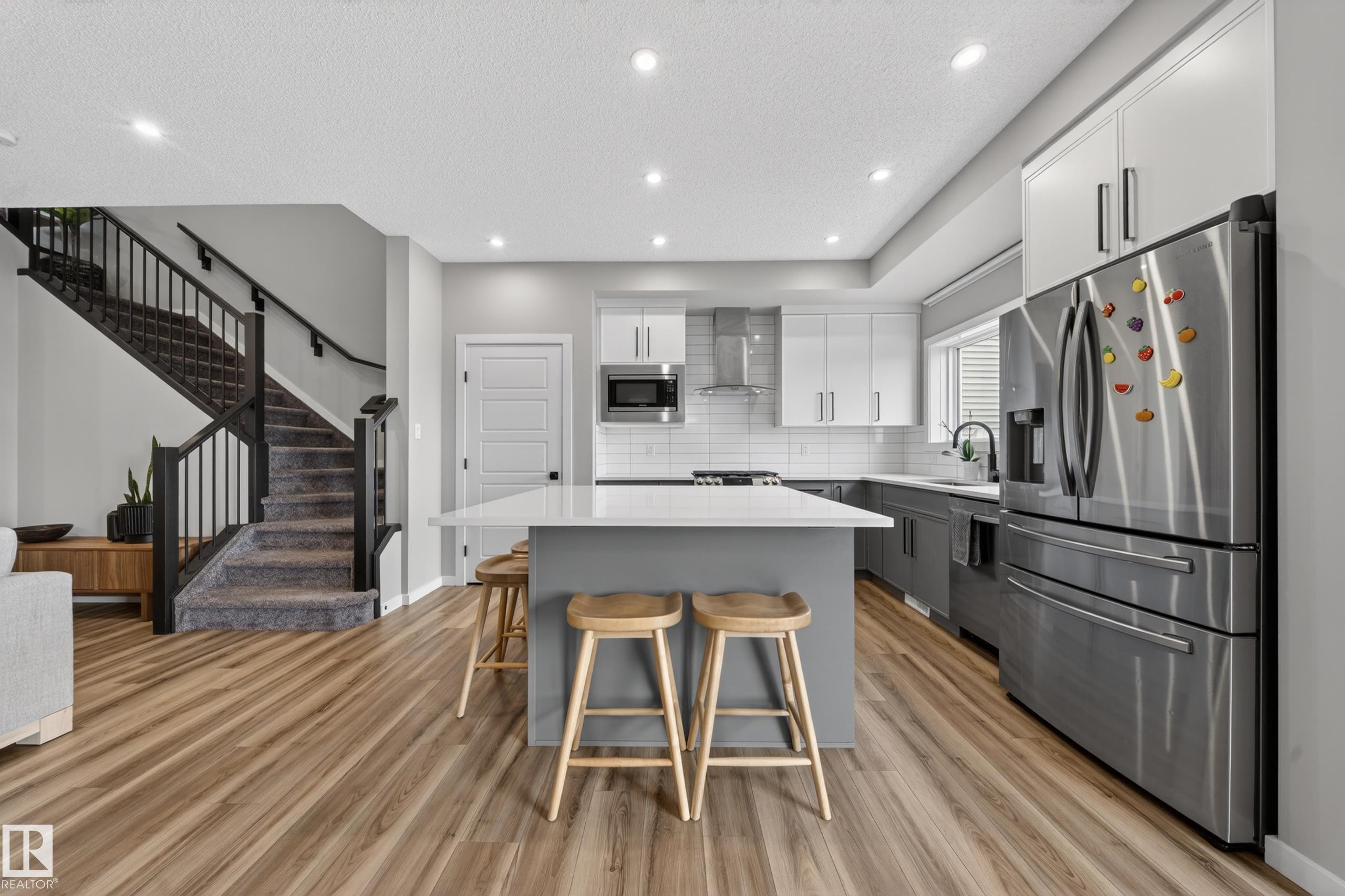 Open-concept kitchen featuring an oversized island with seating, stainless steel appliances, and wood-finish flooring - 3337 Kulay Way, Edmonton, AB - Indoor Photo Showing Kitchen With Upgraded Kitchen
