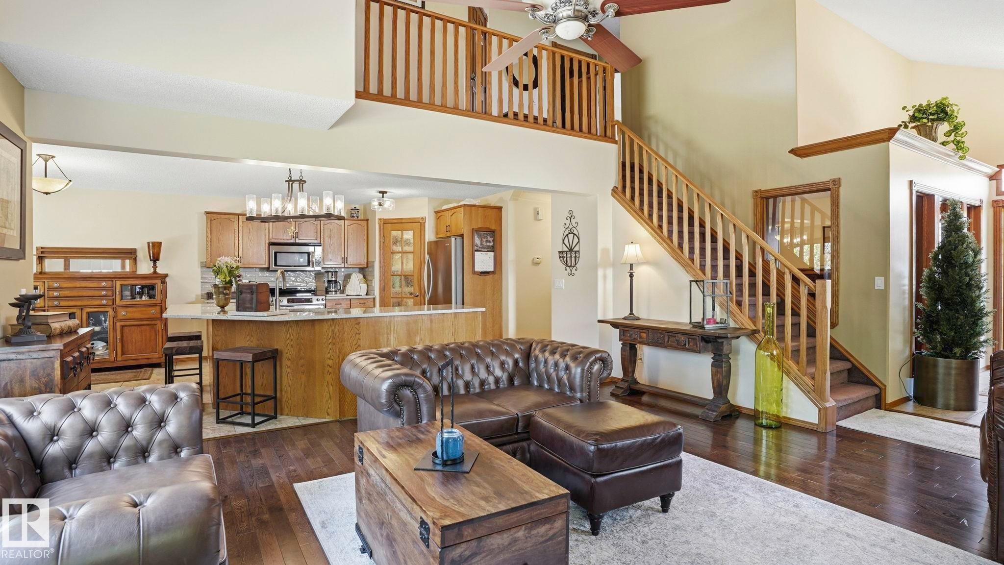 Open-concept living space featuring wood-finish flooring, a two-story ceiling, a staircase with wood railing, a kitchen island with seating, and wood cabinetry - 4309 37A Avenue, Edmonton, AB - Indoor Photo Showing Living Room