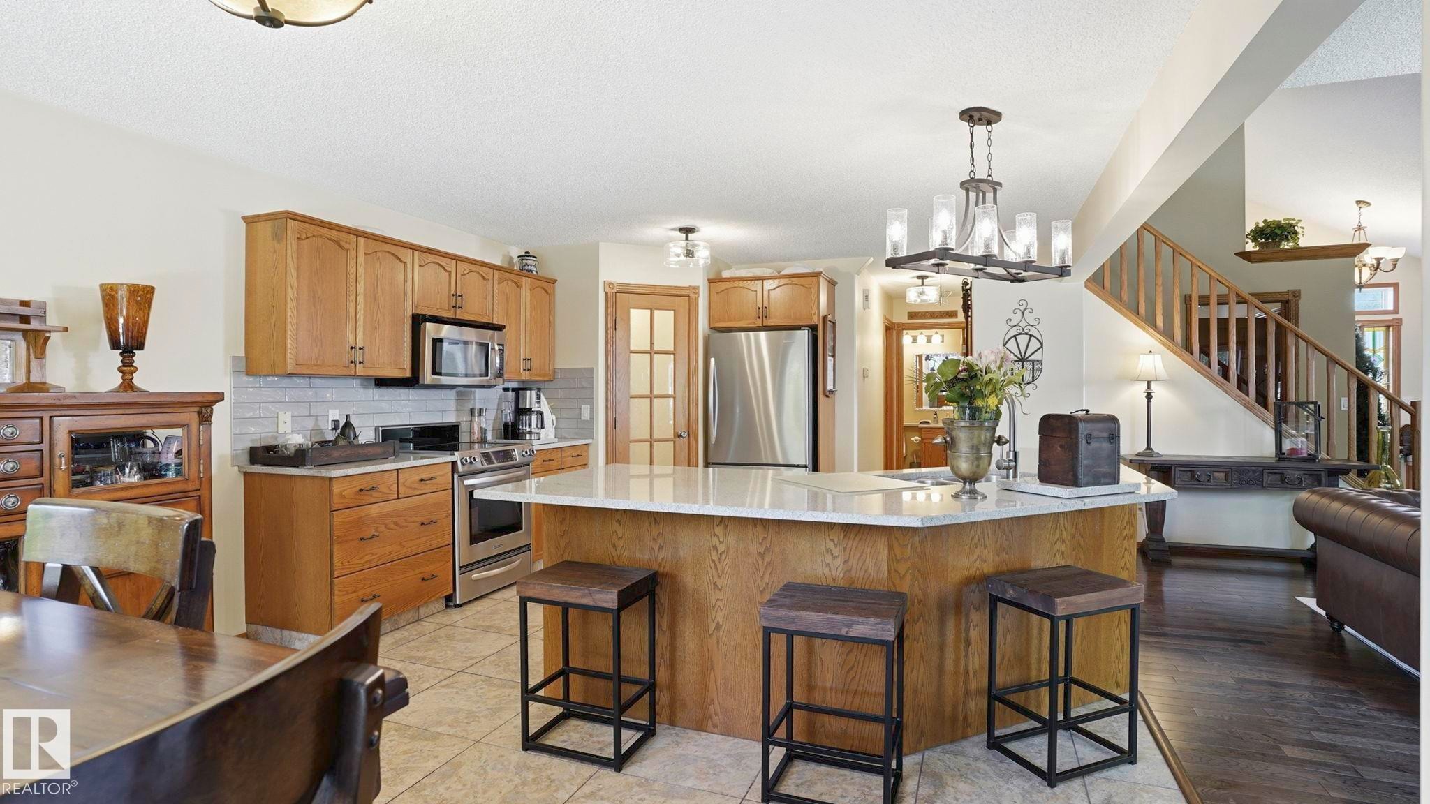 Spacious kitchen featuring an angled island with seating, stainless steel appliances, wood cabinetry, tile flooring, and a subway tile backsplash - 4309 37A Avenue, Edmonton, AB - Indoor Photo Showing Kitchen