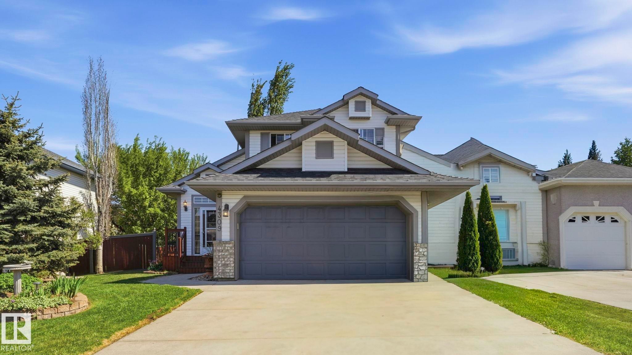 Two-story residence featuring a two-car garage with stone accents, a concrete driveway, and a front yard with manicured lawn and mature trees - 4309 37A Avenue, Edmonton, AB - Outdoor With Facade