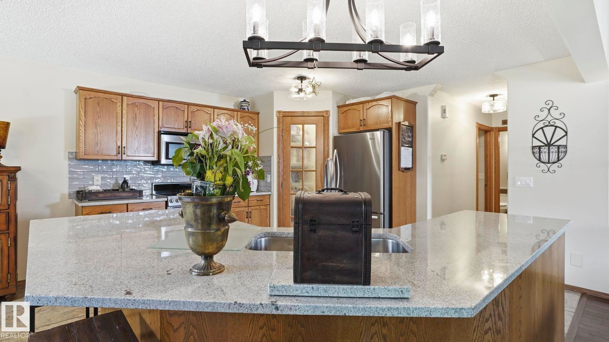 Kitchen featuring a large central island with a built-in sink, light-toned countertops, wood cabinetry, and stainless steel appliances - 4309 37A Avenue, Edmonton, AB - Indoor Photo Showing Kitchen With Upgraded Kitchen