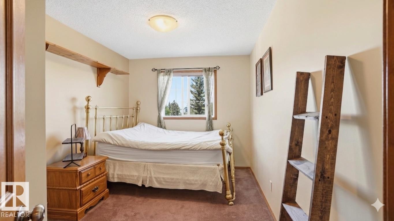 Bedroom featuring a window with exterior tree scenery, soft beige wall paint, ceiling-mounted light fixture, and brown carpet flooring - 4309 37A Avenue, Edmonton, AB - Indoor Photo Showing Bedroom