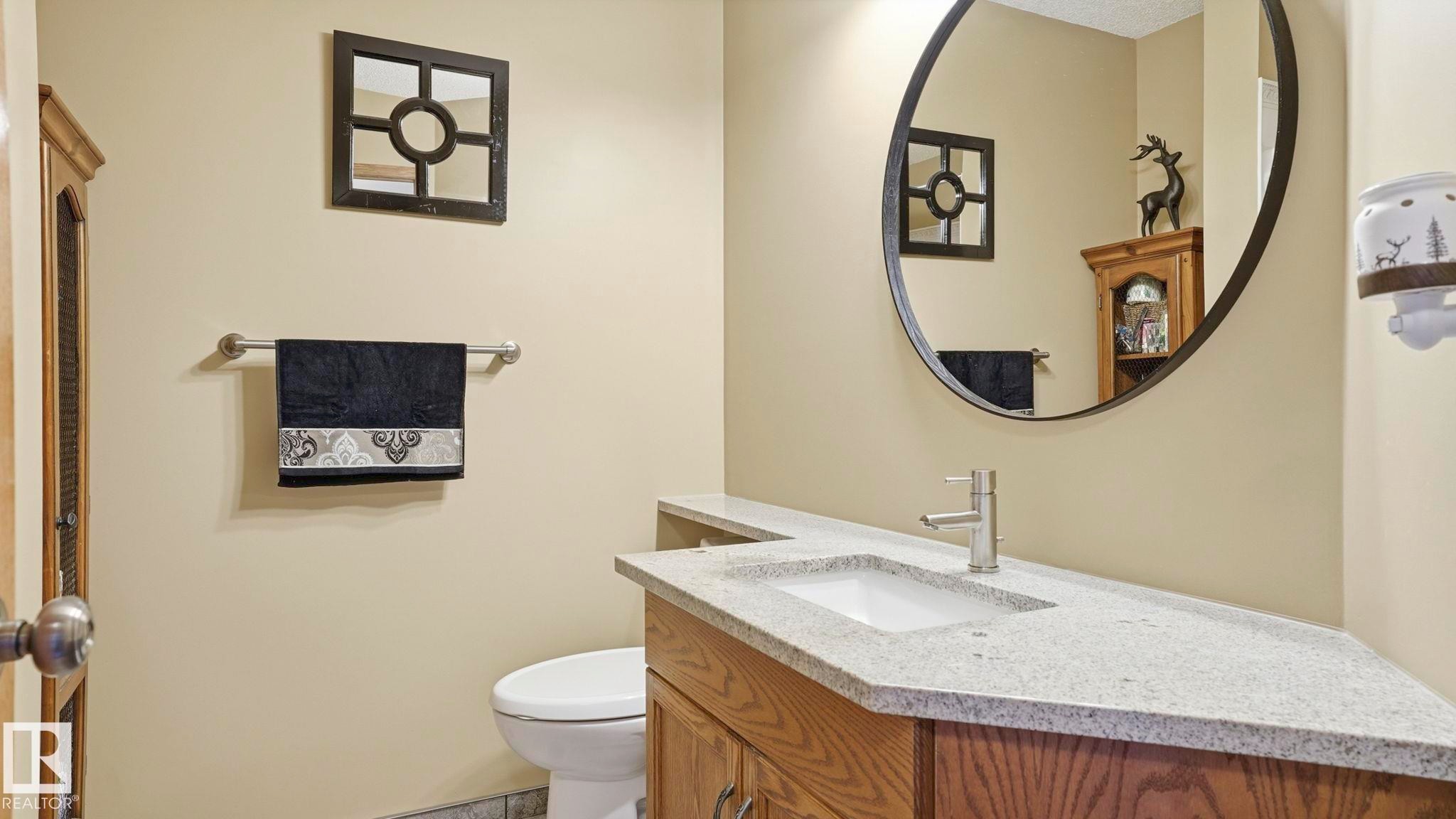 Bathroom featuring a granite-finish countertop, undermount sink, wood-finish vanity, and a large oval mirror - 4309 37A Avenue, Edmonton, AB - Indoor Photo Showing Bathroom