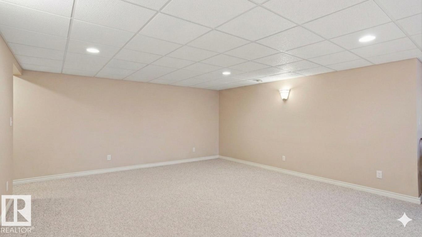 Spacious room featuring neutral carpeting, light beige walls, a drop ceiling with recessed lighting, and a wall sconce providing ambient illumination - 4309 37A Avenue, Edmonton, AB - Indoor