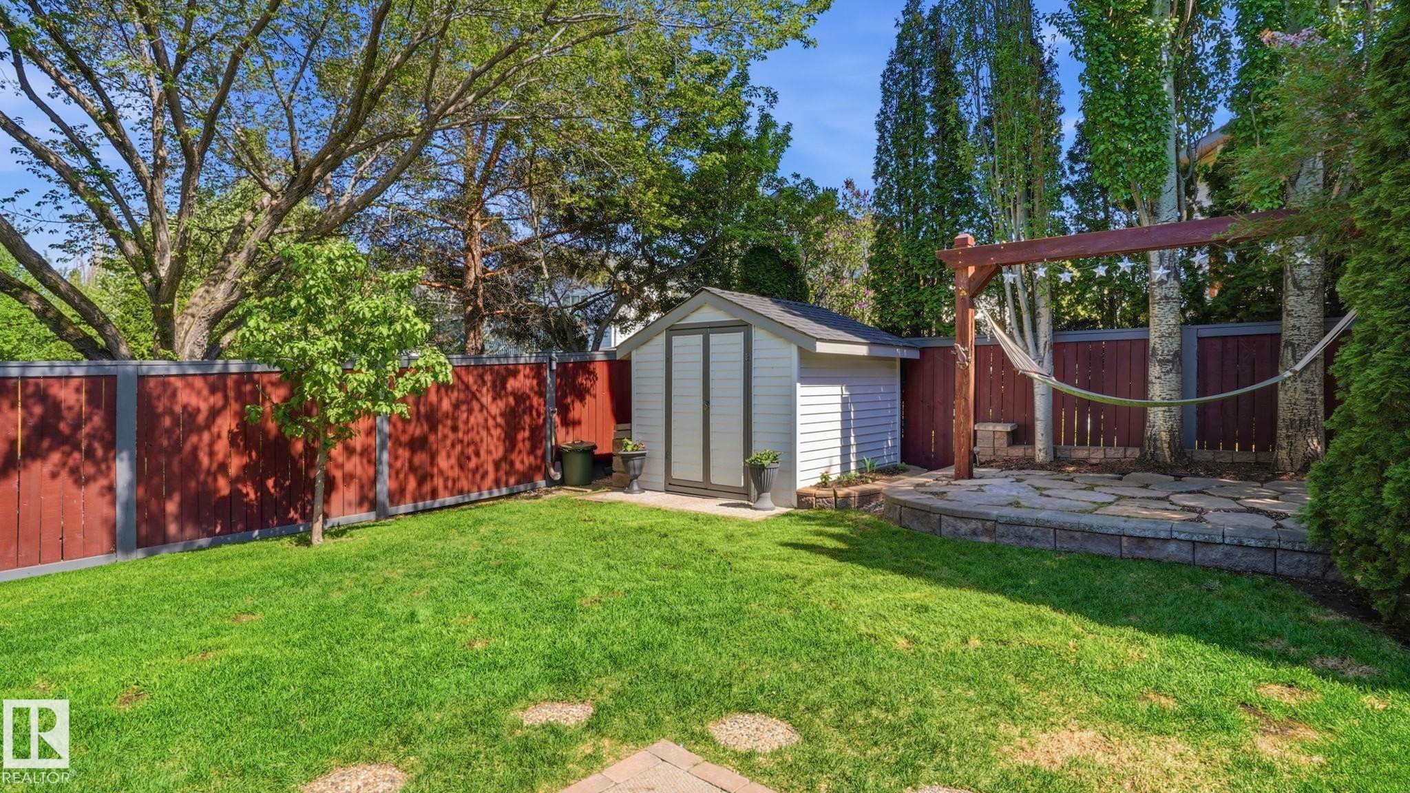 Fenced backyard featuring a manicured lawn, stone patio, storage shed, and a wooden pergola structure - 4309 37A Avenue, Edmonton, AB - Outdoor