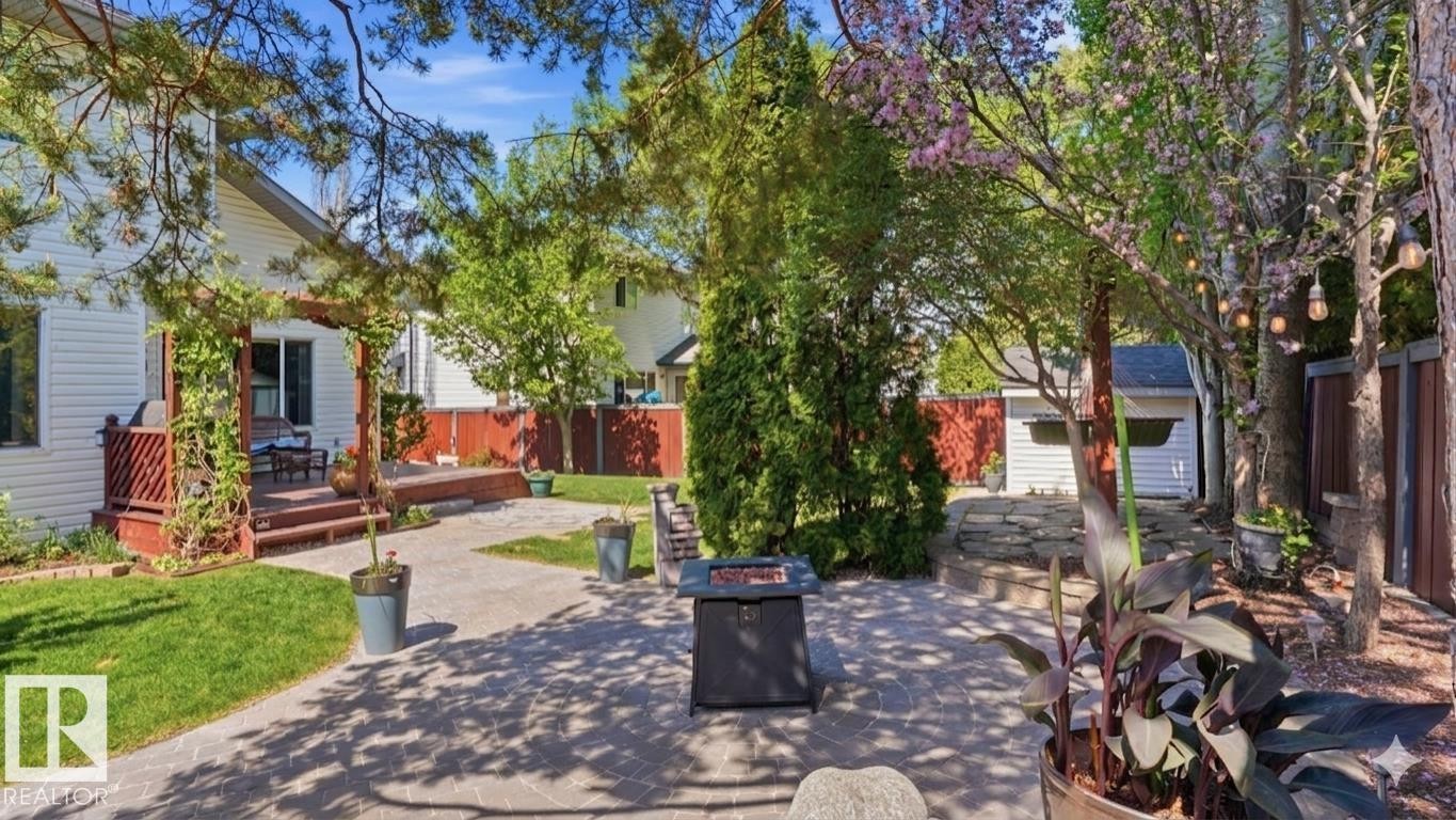 Paver patio featuring a fire pit, bordered by a wooden deck with a pergola, and surrounded by mature trees and shrubs - 4309 37A Avenue, Edmonton, AB - Outdoor