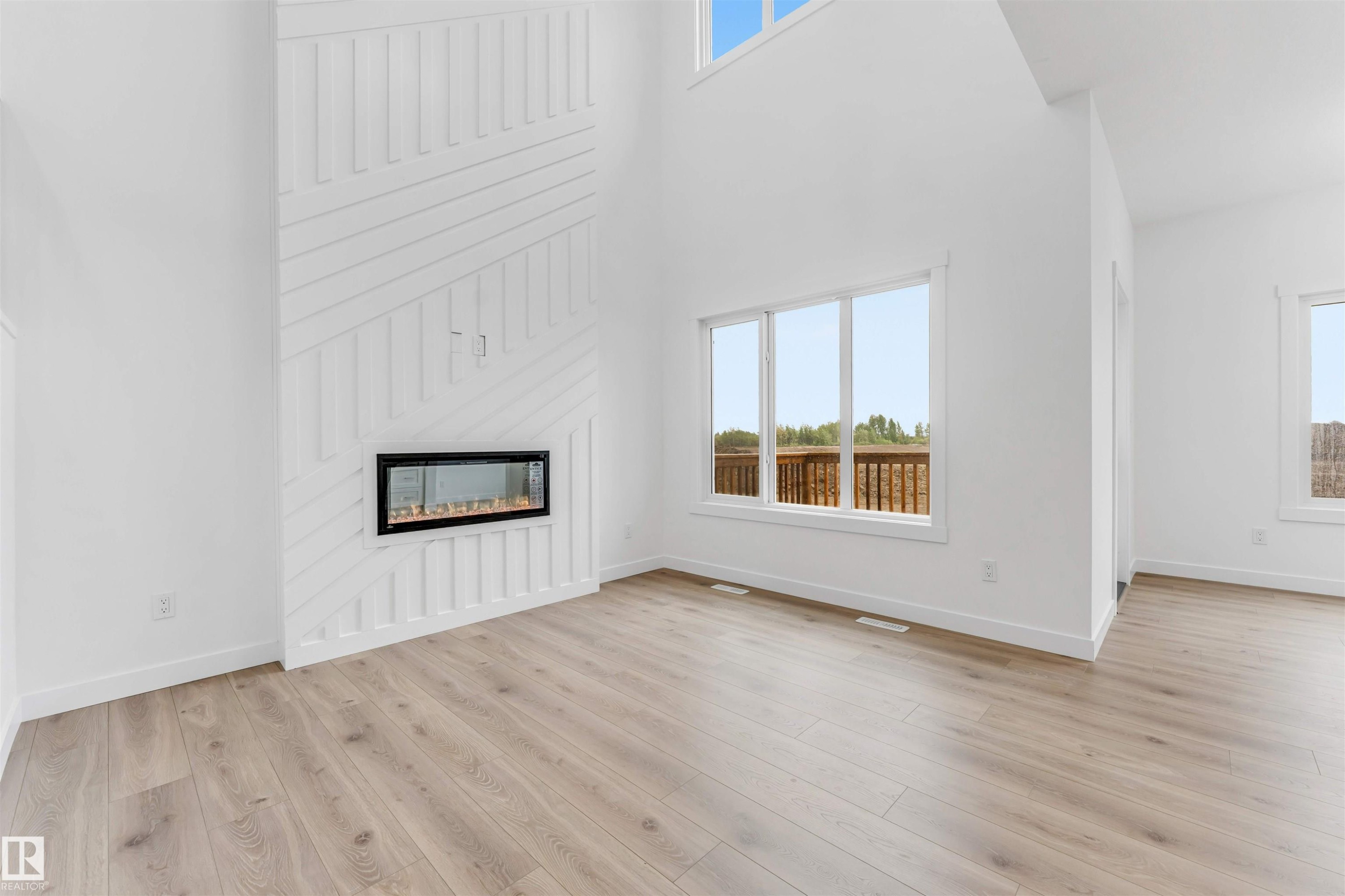Living area featuring a floor-to-ceiling accent wall with a linear electric fireplace, high ceilings, large windows, and wood-finish flooring - 1972 210 Street, Edmonton, AB - Indoor Photo Showing Other Room With Fireplace