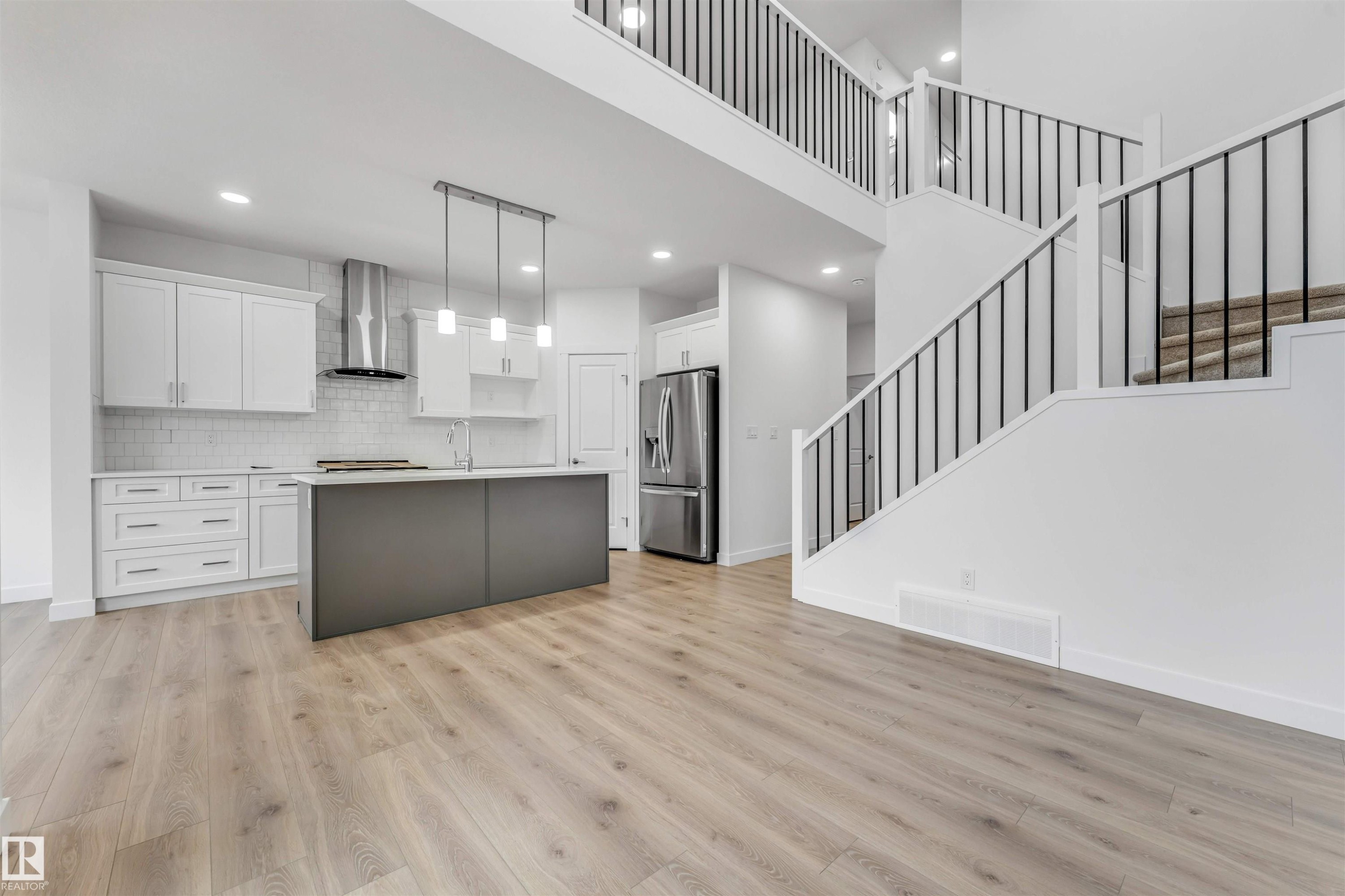 Open-concept living area featuring wood-finish flooring, a contemporary kitchen, and a double-height ceiling - 1972 210 Street, Edmonton, AB - Indoor Photo Showing Kitchen With Upgraded Kitchen