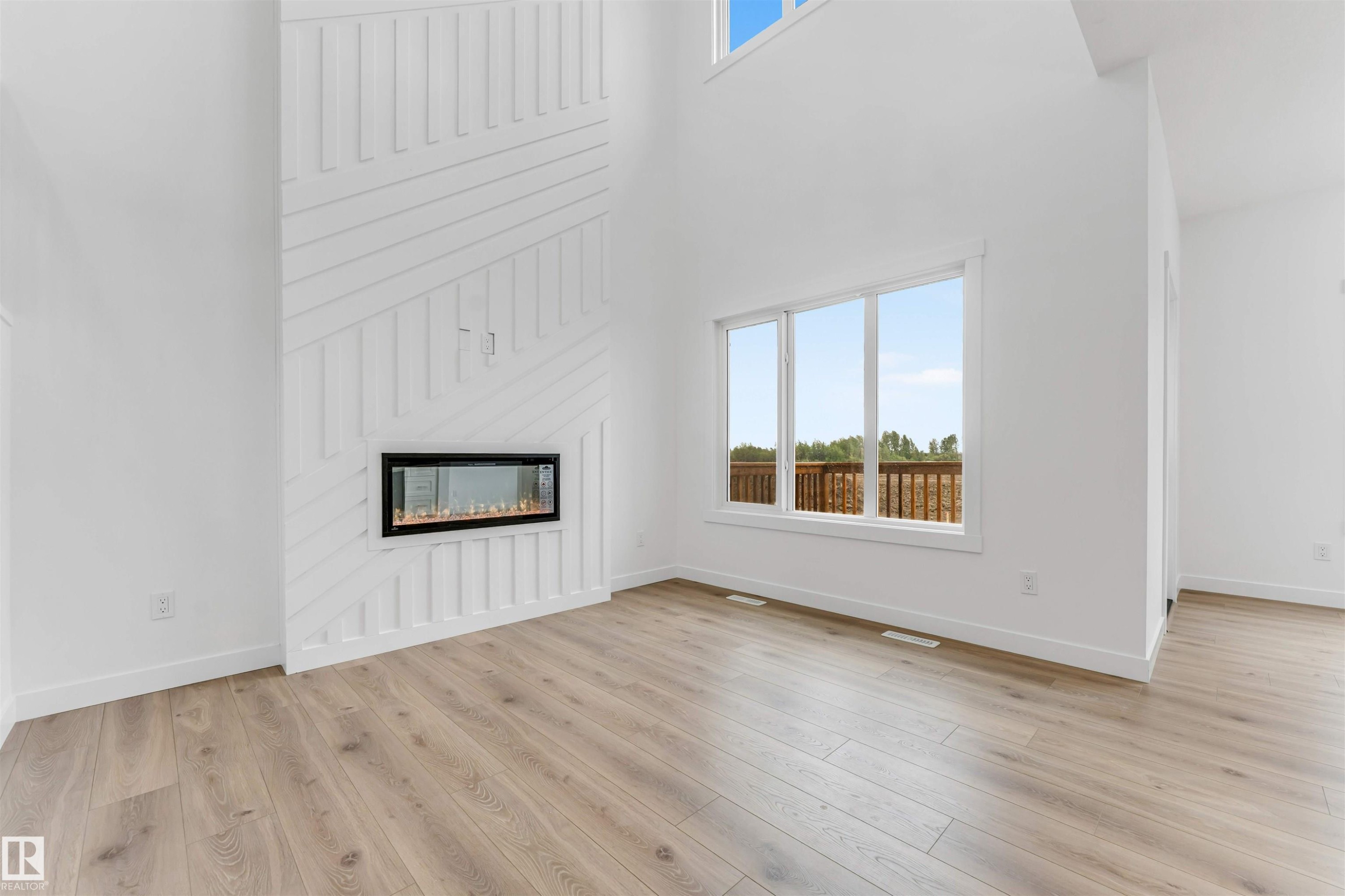 Spacious interior featuring a linear electric fireplace with a decorative shiplap surround, high ceilings, multiple windows, and wood-finish flooring - 1972 210 Street, Edmonton, AB - Indoor With Fireplace