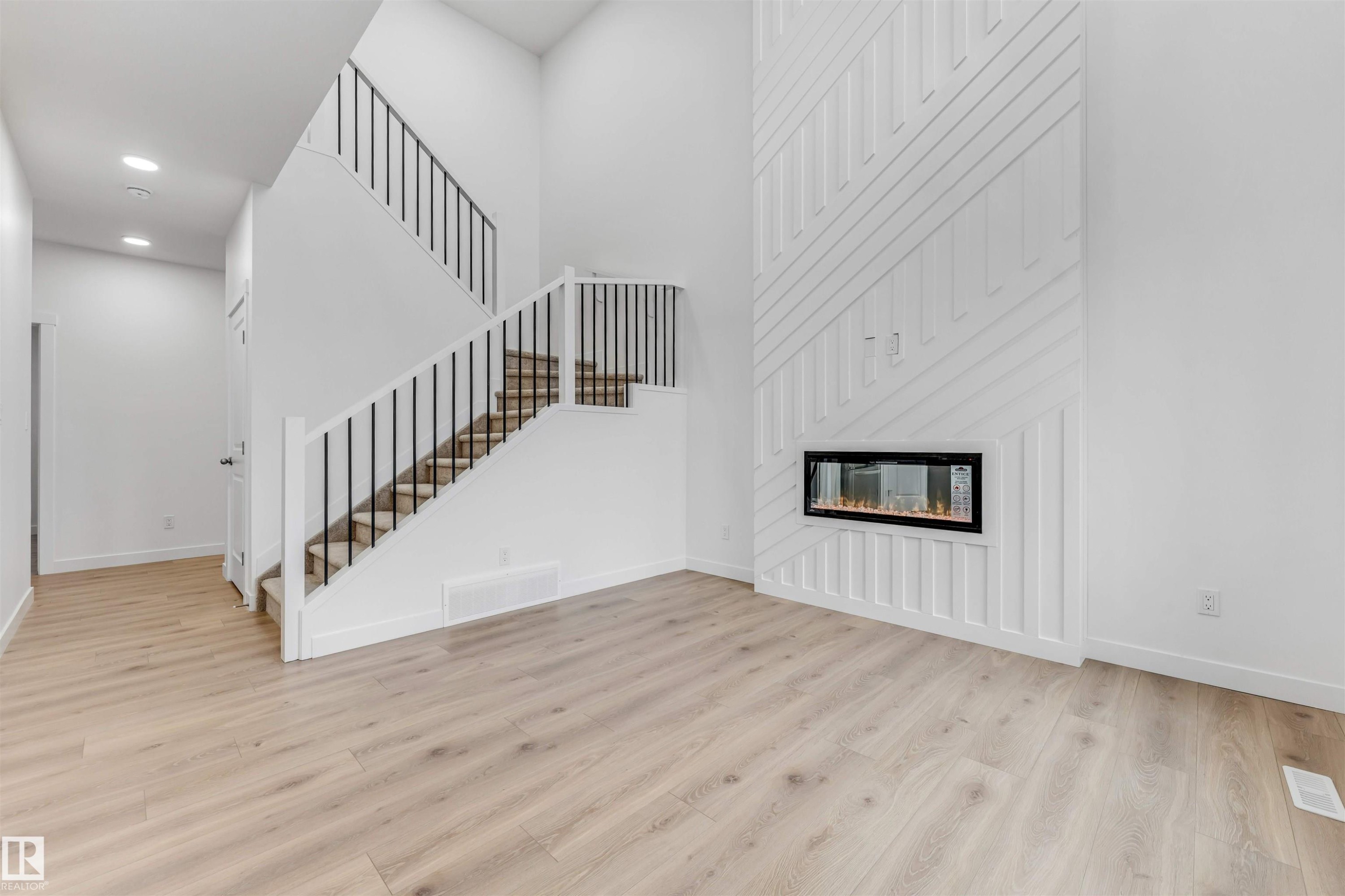 High ceilings complement this open living space featuring wood-finish flooring and a contemporary linear fireplace - 1972 210 Street, Edmonton, AB - Indoor With Fireplace