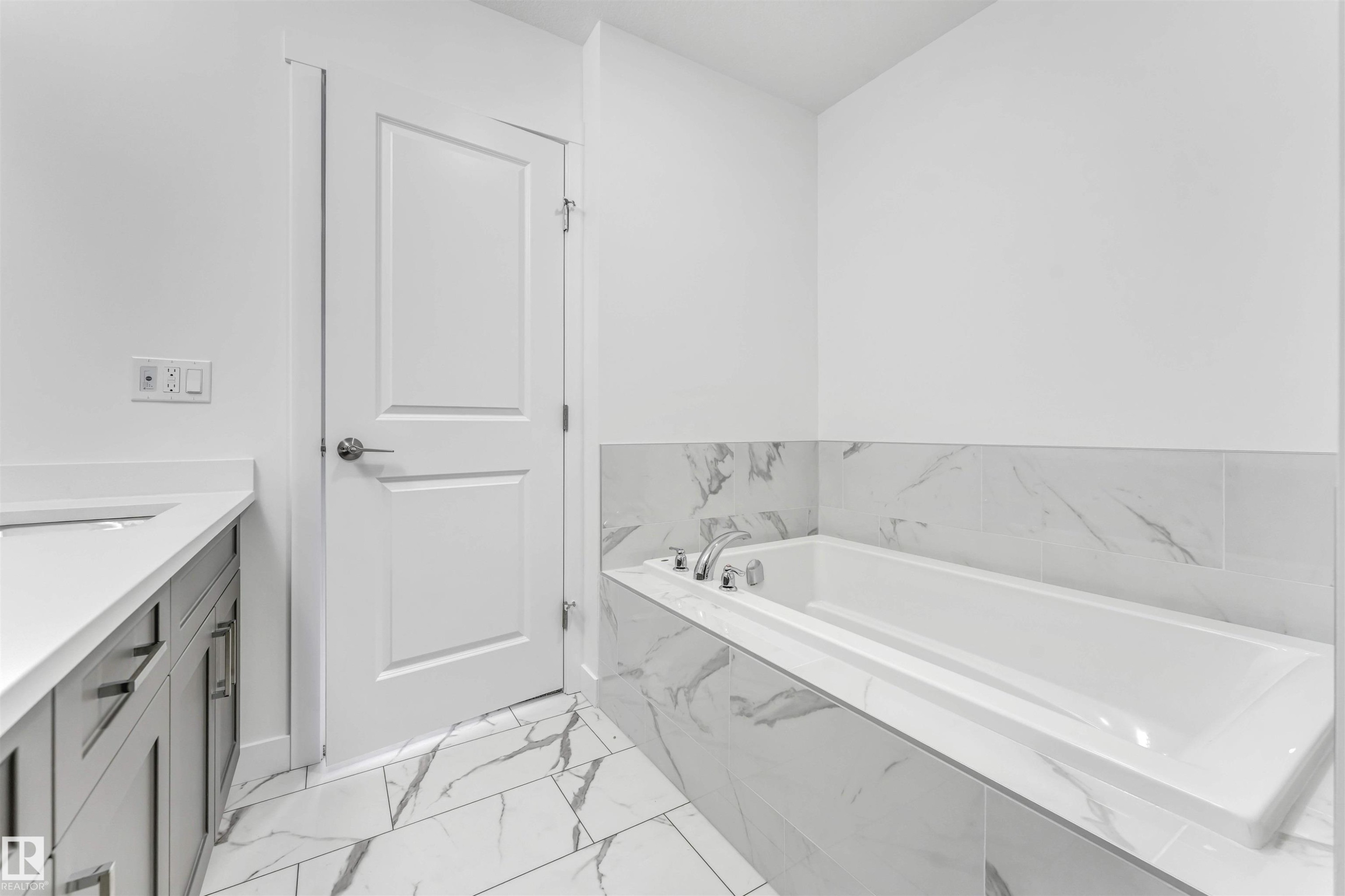 Soaking tub with surrounding tilework, complemented by a vanity with an integrated sink and light gray cabinetry - 1972 210 Street, Edmonton, AB - Indoor Photo Showing Bathroom