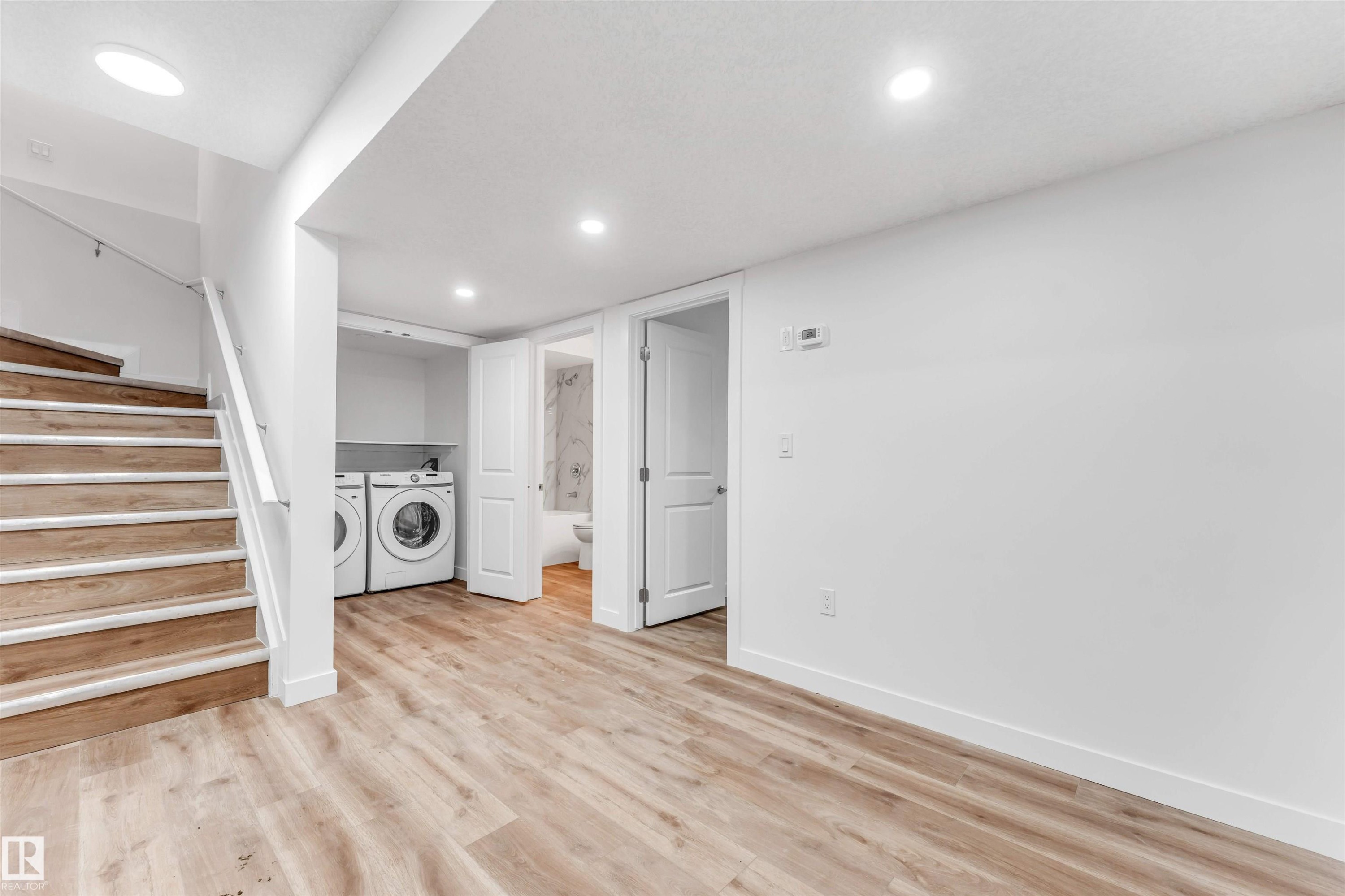 Spacious lower-level area with wood-finish flooring, recessed lighting, and a contemporary white staircase - 1972 210 Street, Edmonton, AB - Indoor Photo Showing Laundry Room