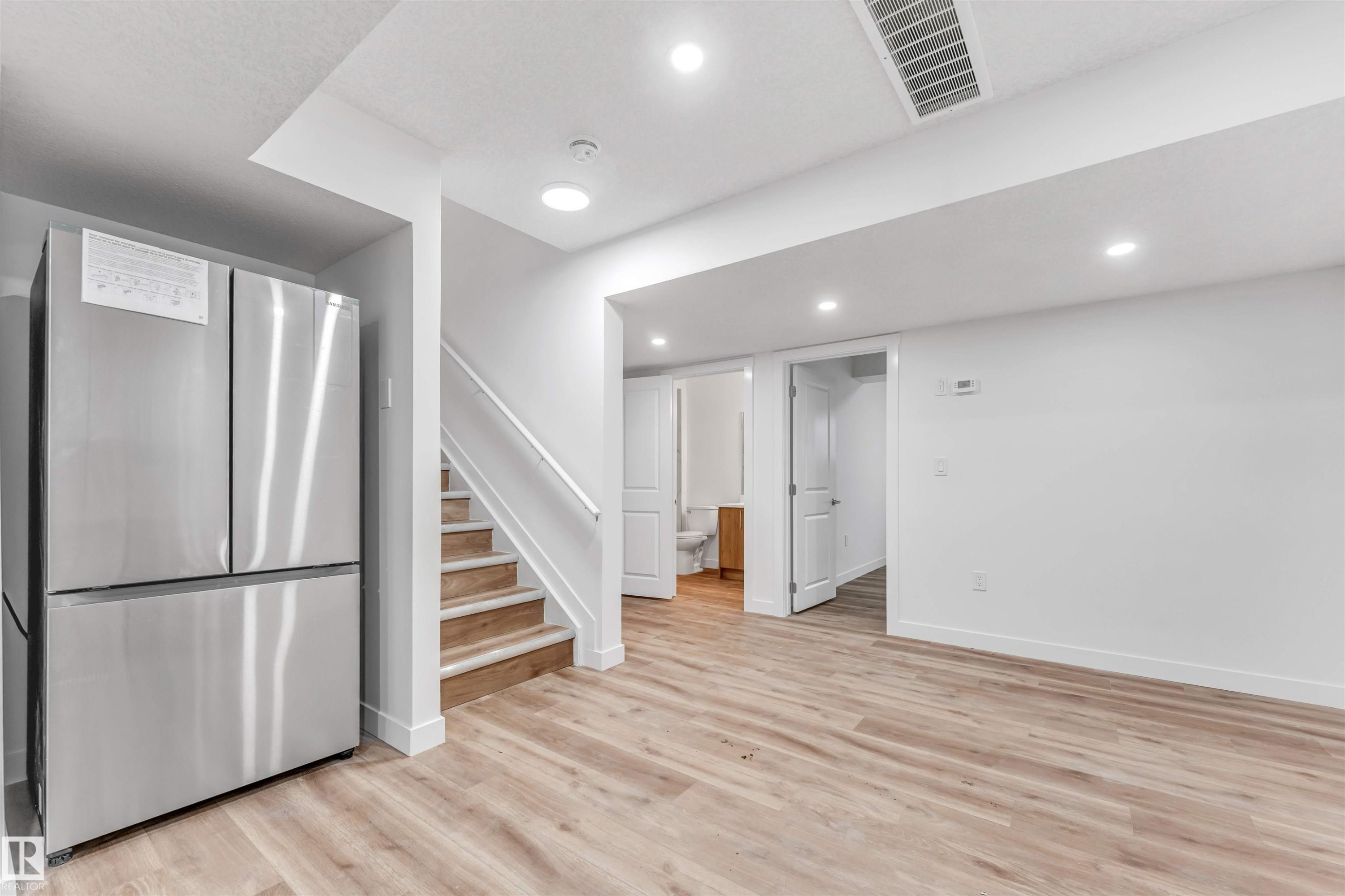 Open-concept space featuring light wood-finish flooring, recessed lighting, and a modern stainless steel refrigerator - 1972 210 Street, Edmonton, AB - Indoor Photo Showing Other Room