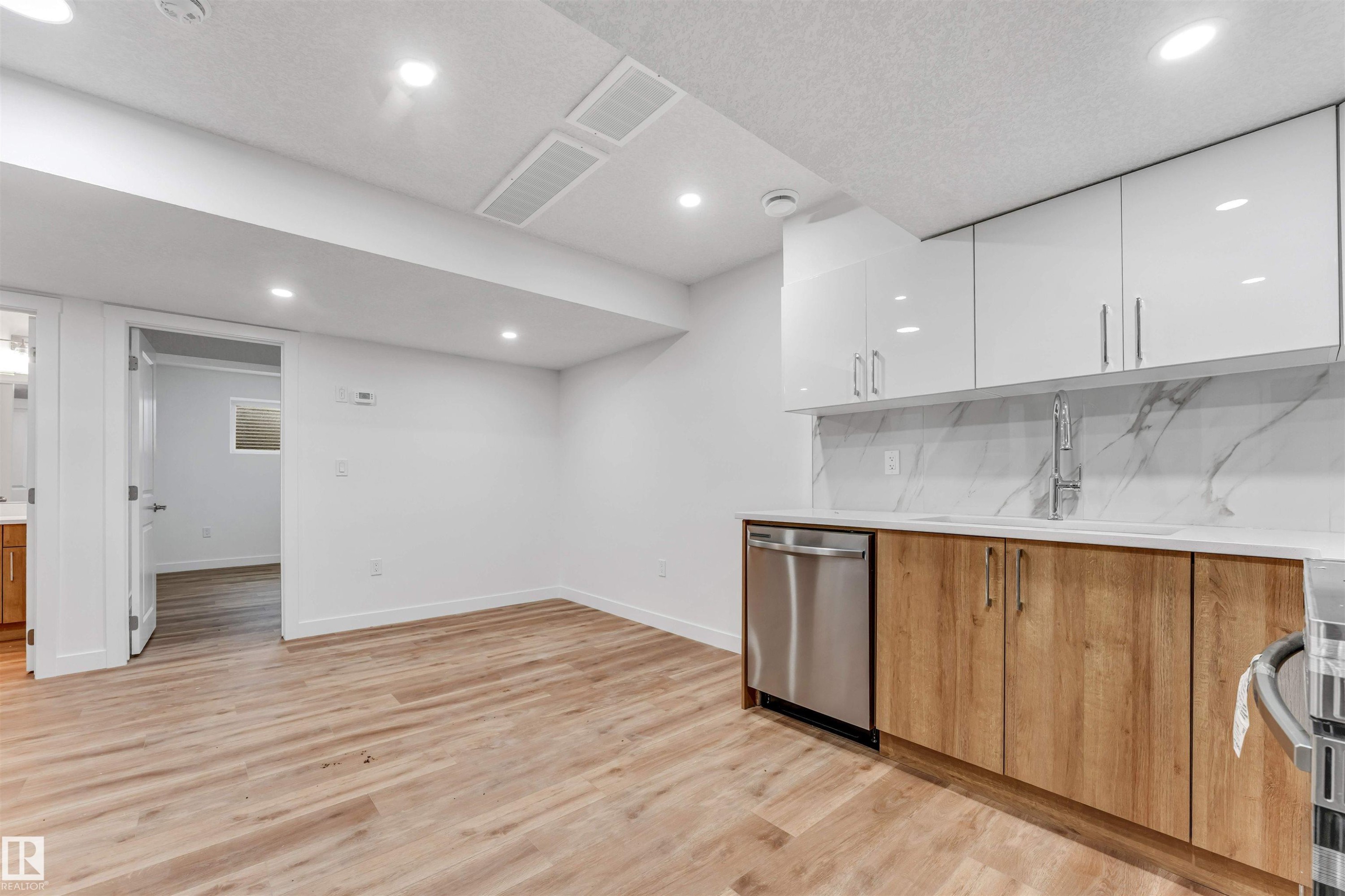 Modern kitchen area featuring stainless steel dishwasher, wood-finish lower cabinetry, white upper cabinetry, and a white countertop with a matching backsplash - 1972 210 Street, Edmonton, AB - Indoor