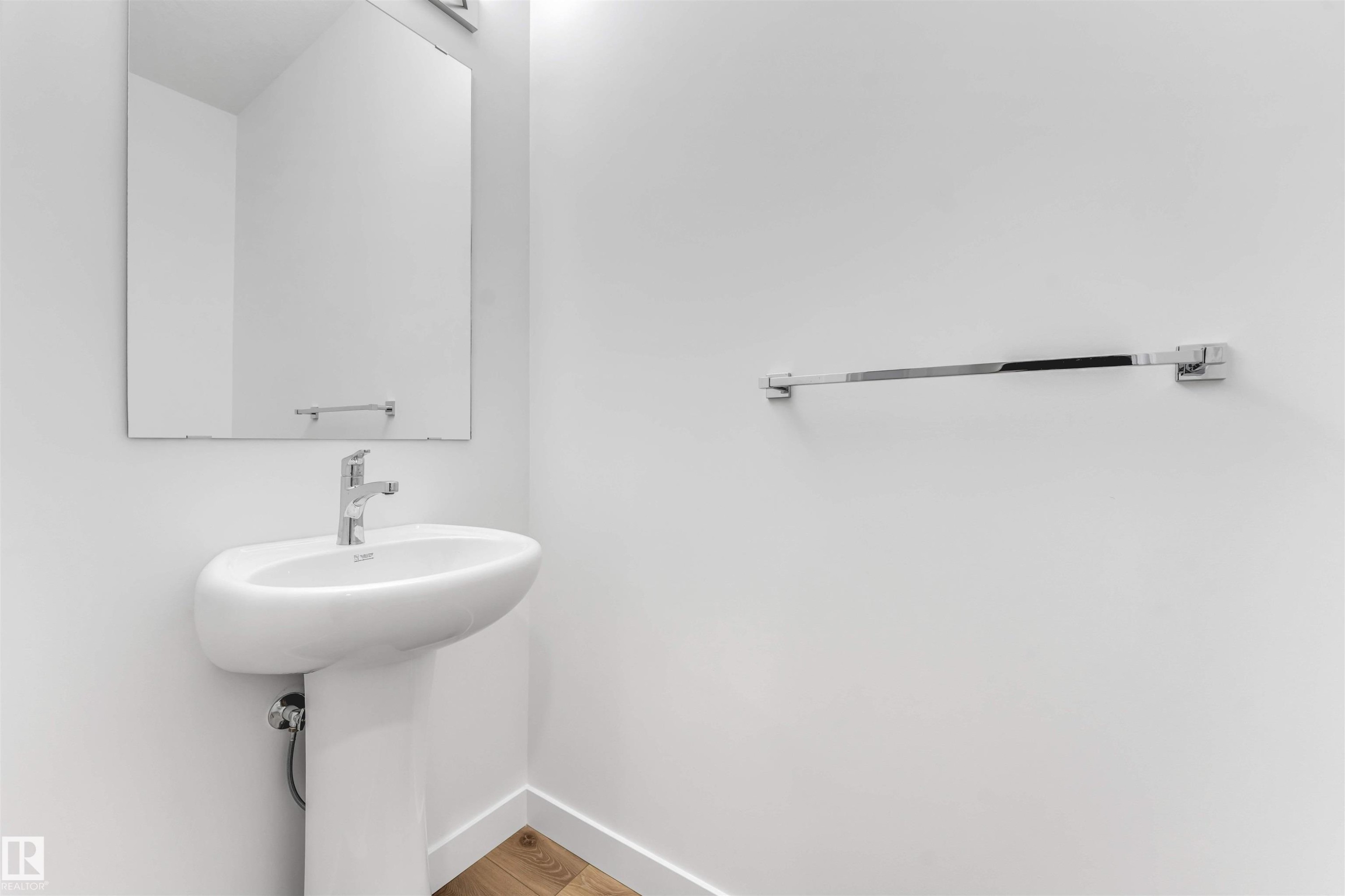 White pedestal sink with a contemporary chrome faucet, framed mirror, chrome towel bar, and wood-finish flooring - 1972 210 Street, Edmonton, AB - Indoor Photo Showing Bathroom
