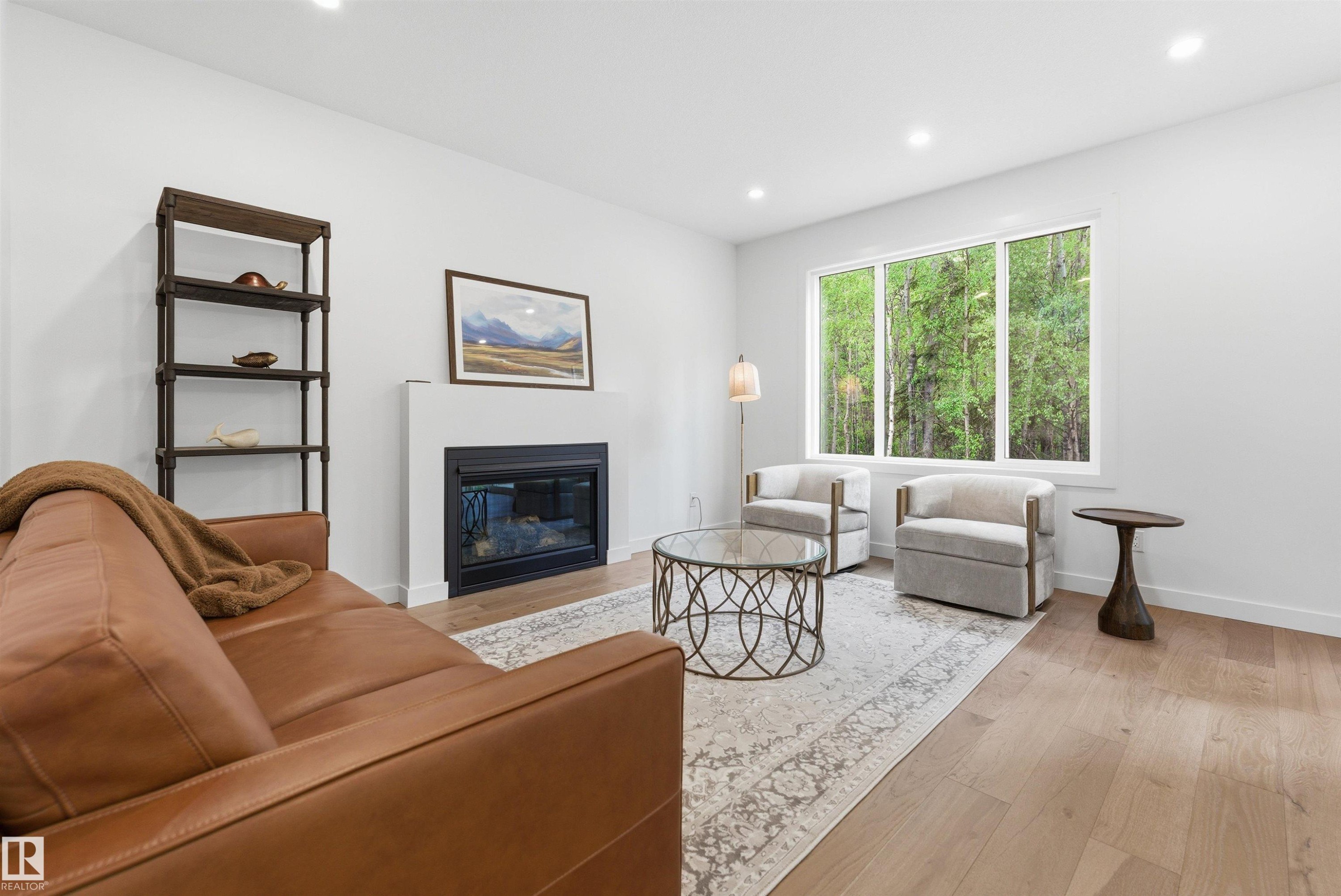 Spacious living area featuring light wood-finish flooring, a contemporary fireplace with a white mantel, and large windows providing abundant natural light - 132 Heron Point Close, Rural Wetaskiwin County, AB