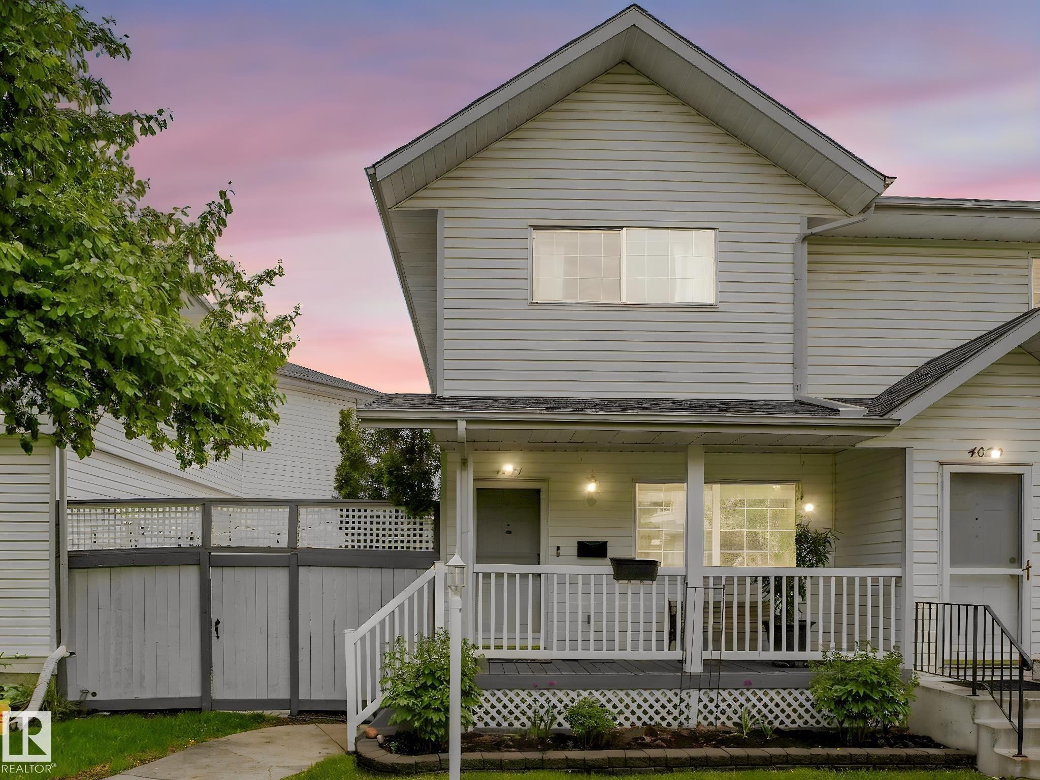 Exterior featuring white siding, a covered front porch with white railings, a front entry with a black metal handrail, and a decorative lattice skirt - 4031 38 Street, Edmonton, AB