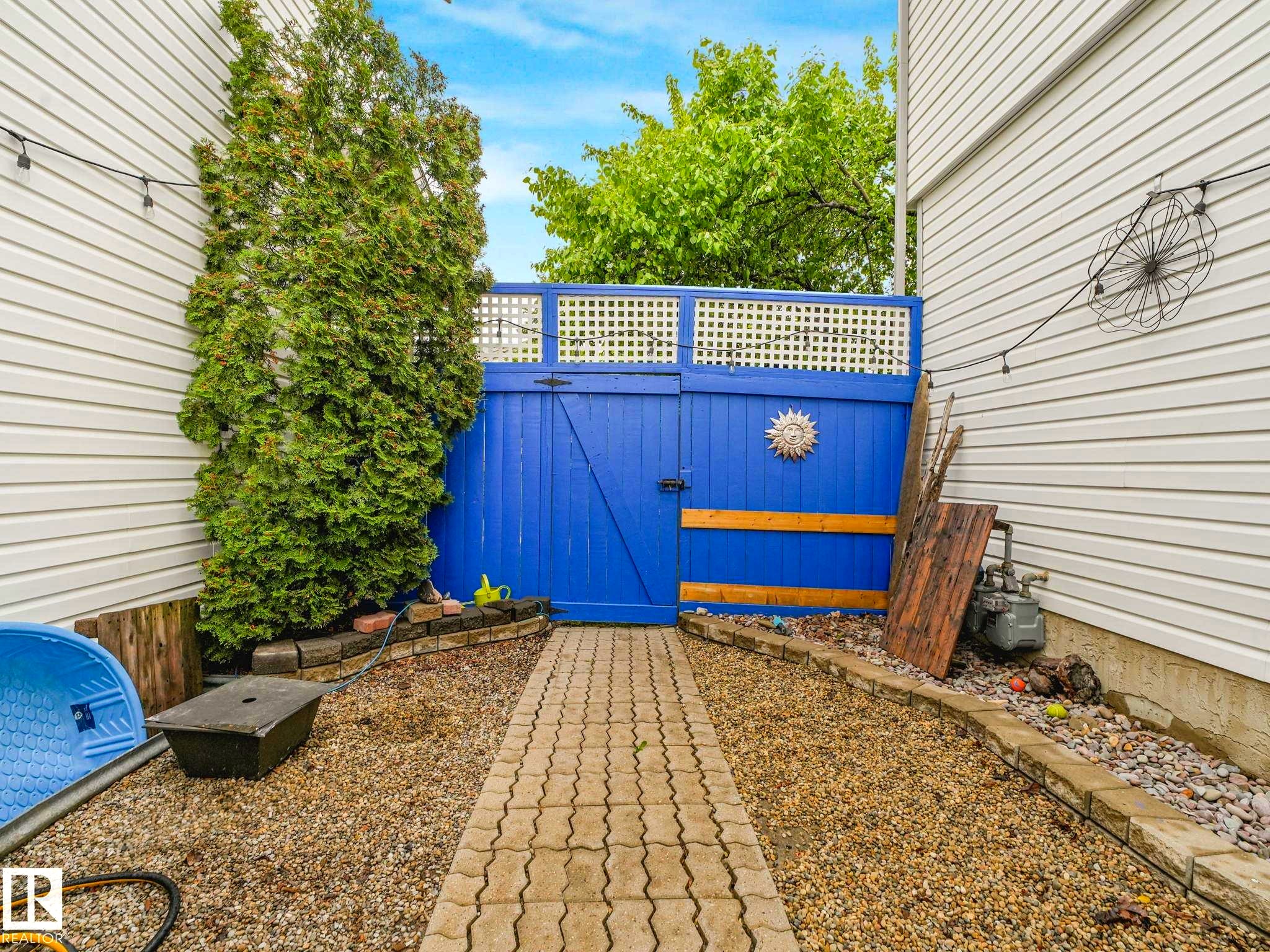 Path with paver stones leading to a blue wooden gate with white lattice detailing - 4031 38 Street, Edmonton, AB