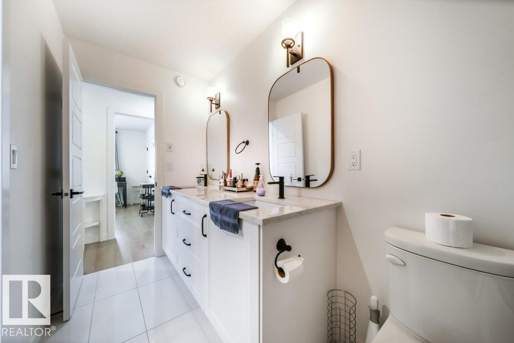 Double vanity featuring white cabinetry with black hardware, stone countertop, two rectangular mirrors, and wall-mounted sconces - 11303 111 Avenue, Edmonton, AB - Indoor Photo Showing Bathroom