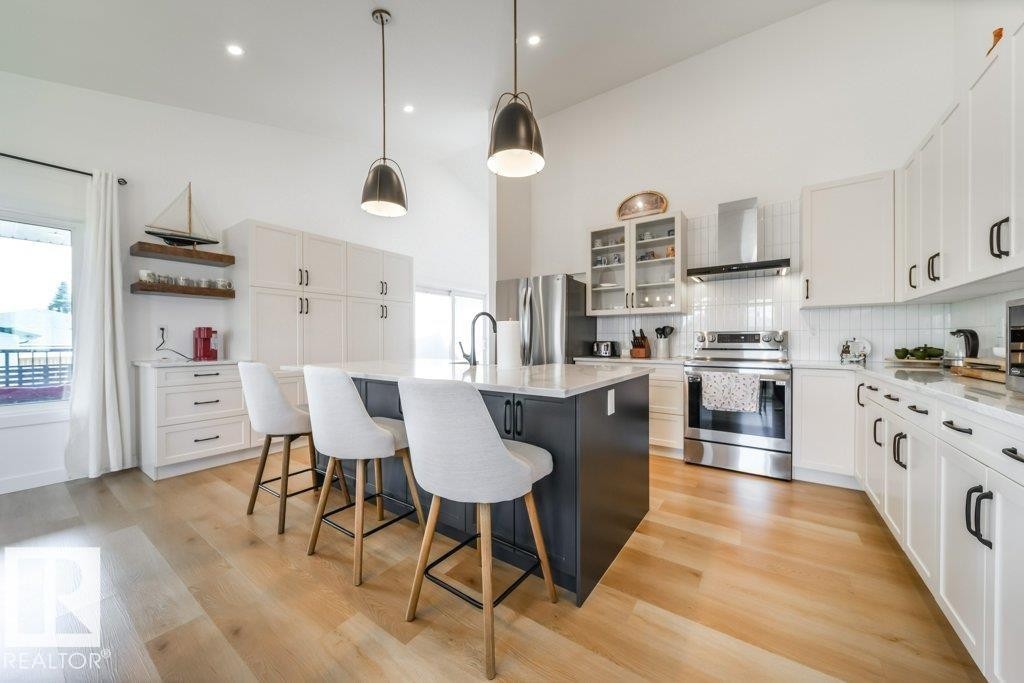 Open-concept kitchen featuring an island with counter seating, stainless steel appliances, white cabinetry with black hardware, and wood-finish flooring - 11303 111 Avenue, Edmonton, AB - Indoor Photo Showing Kitchen With Upgraded Kitchen