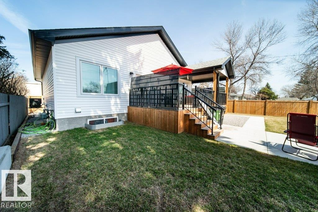Expansive backyard featuring a multi-level deck with black railings, a covered patio area, concrete pathways, and a wooden privacy fence - 11303 111 Avenue, Edmonton, AB - Outdoor