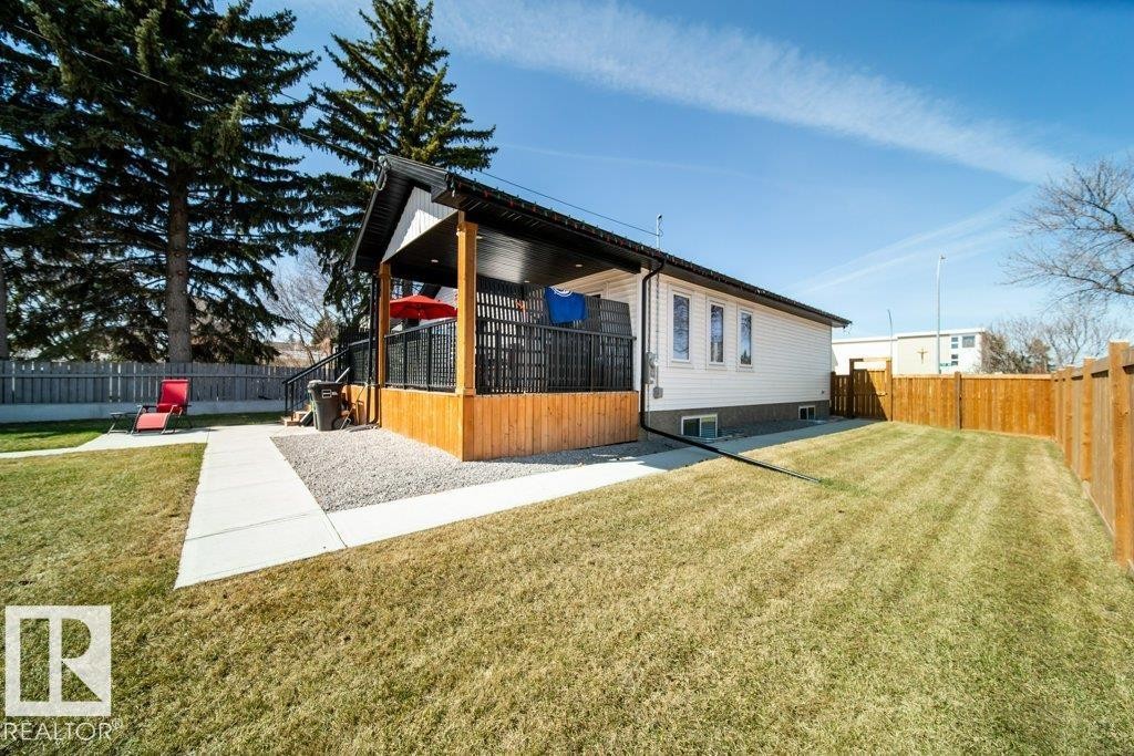 Rear exterior featuring a covered deck with dark railing, a concrete pathway, a gravel patio area, a wood fence, and a spacious lawn - 11303 111 Avenue, Edmonton, AB - Outdoor
