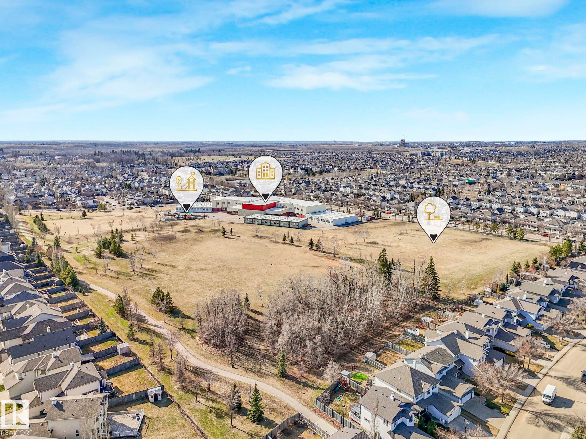 Aerial perspective showcasing suburban development with residential properties, a large open field, and institutional buildings - 322 1520 Hammond Gate Nw, Edmonton, AB - Outdoor With View