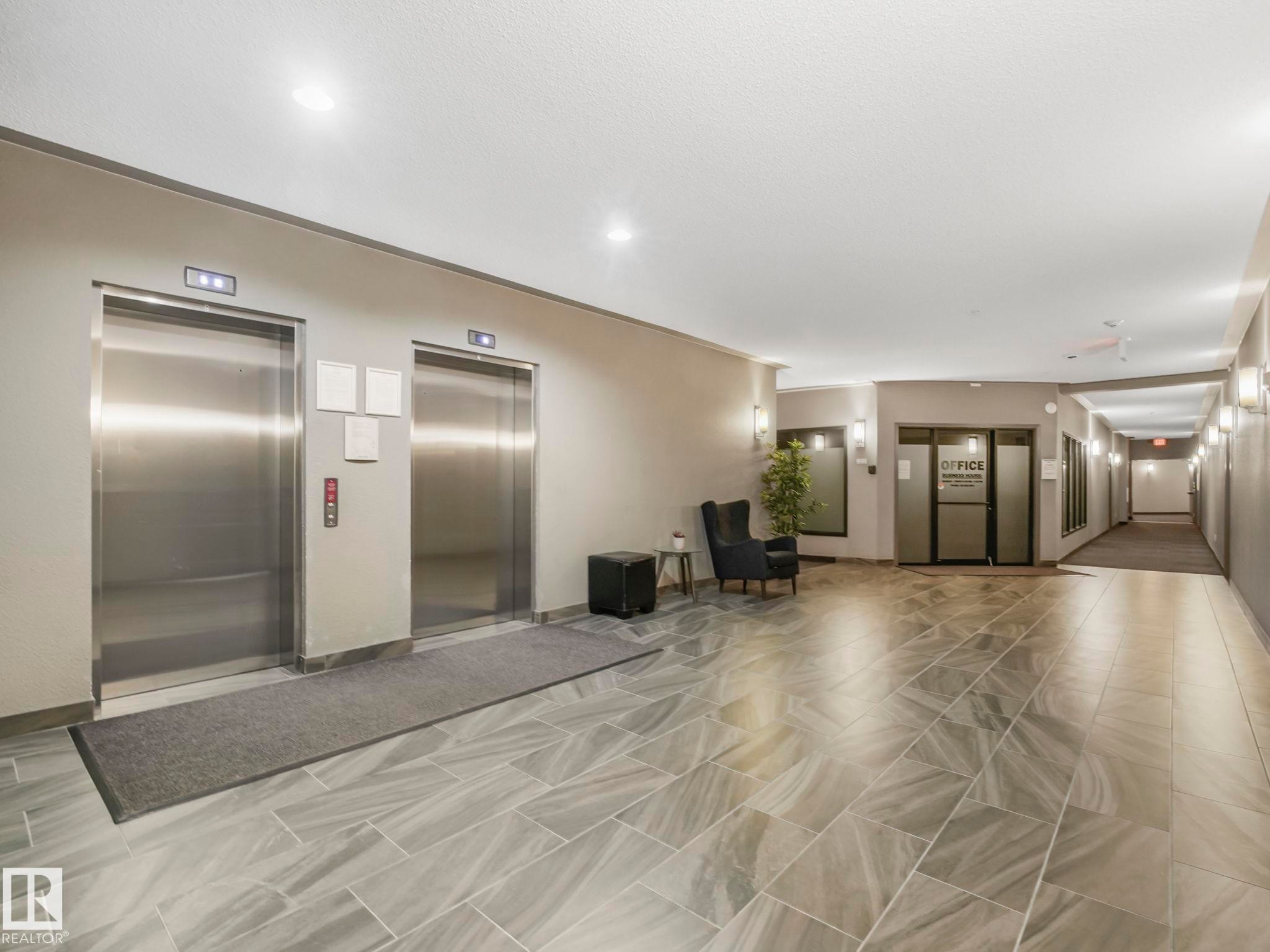 Elevator lobby featuring two stainless steel elevators, overhead recessed lighting, modern sconces, and large format tile flooring - 322 1520 Hammond Gate Nw, Edmonton, AB - Indoor Photo Showing Other Room