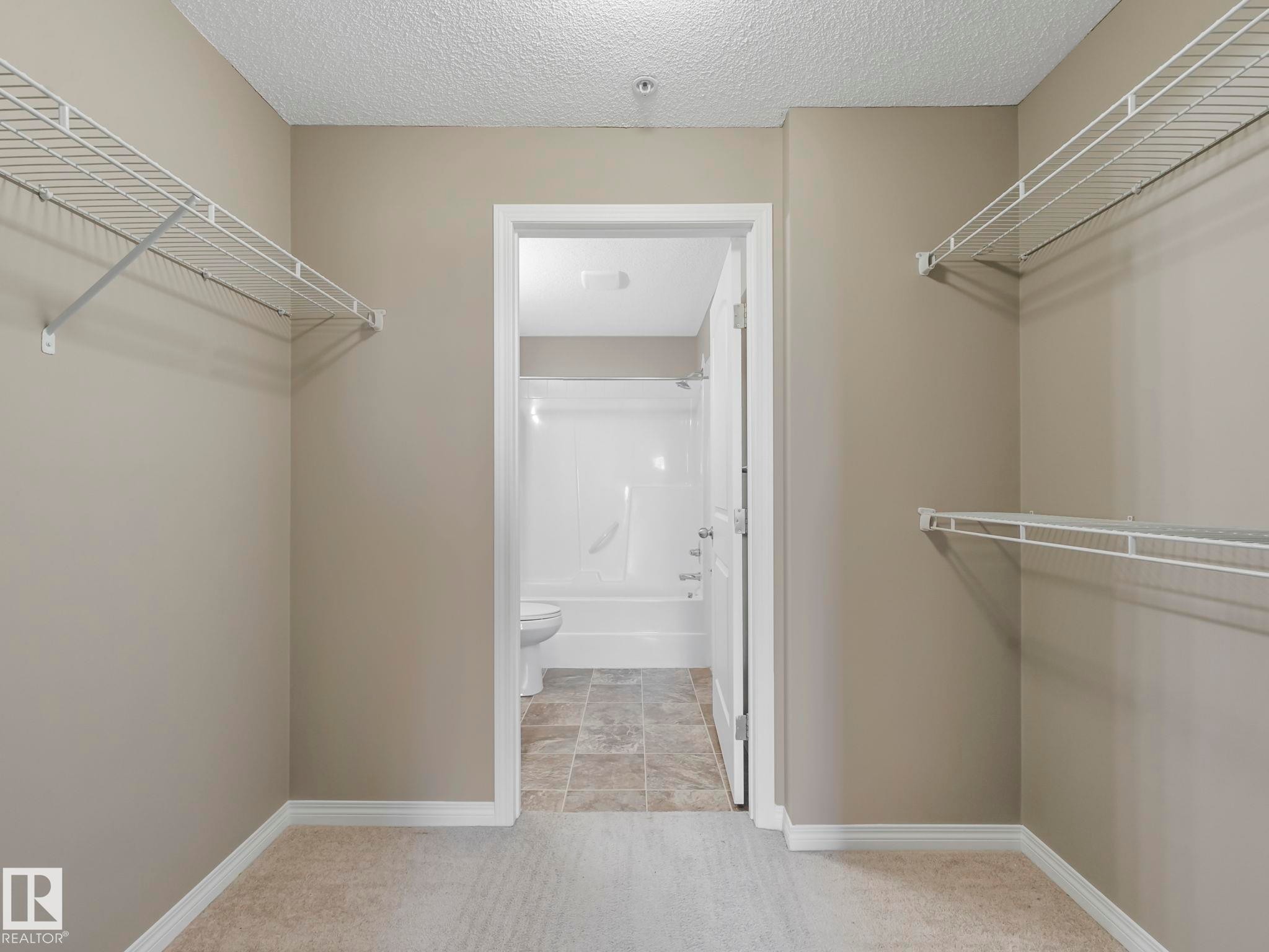 Walk-in closet with carpet flooring, light neutral paint, white wire shelving, and white baseboards - 322 1520 Hammond Gate Nw, Edmonton, AB - Indoor With Storage