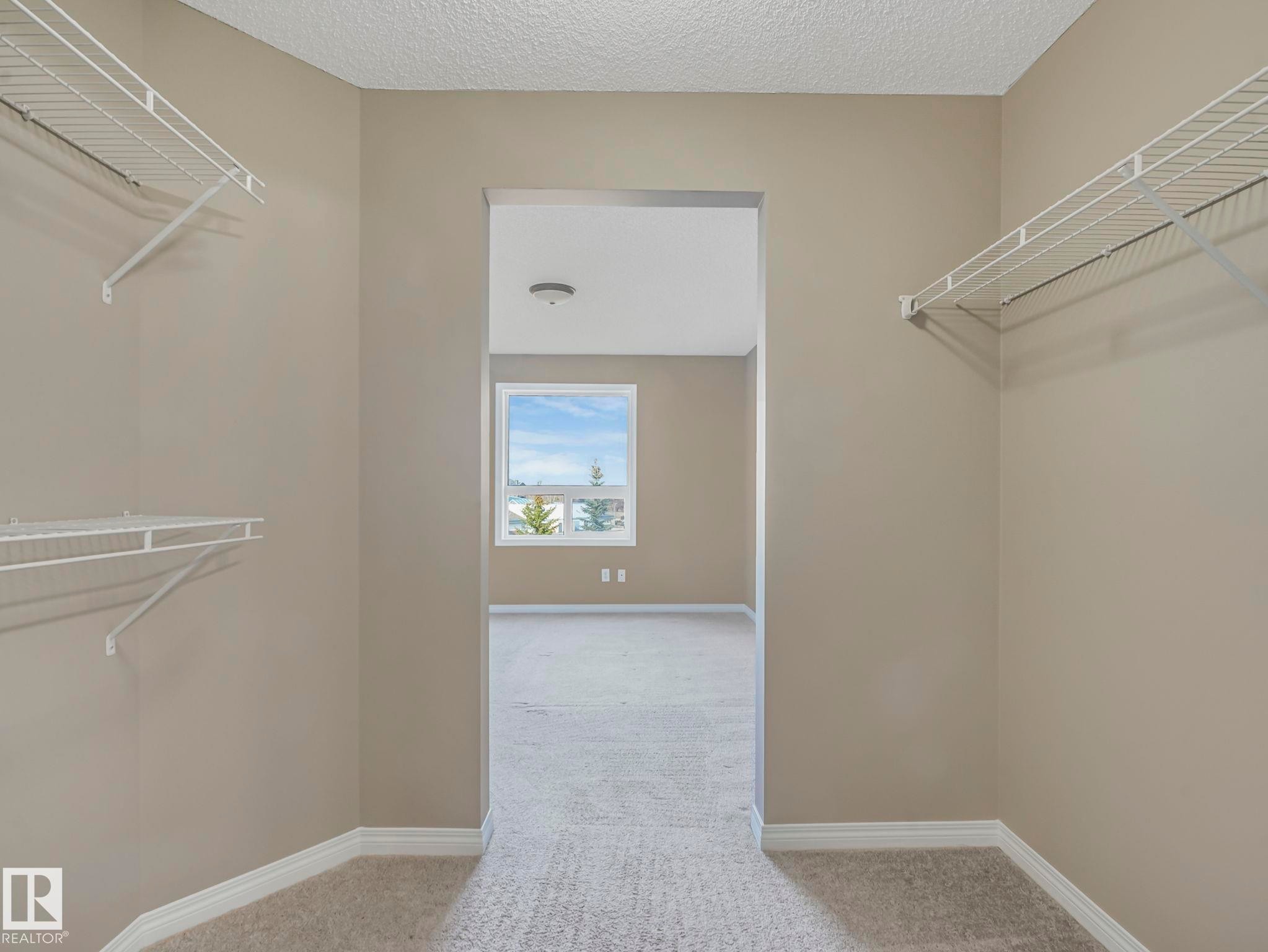 Walk-in closet with neutral-toned walls, white wire shelving, and light-colored carpeting - 322 1520 Hammond Gate Nw, Edmonton, AB - Indoor With Storage