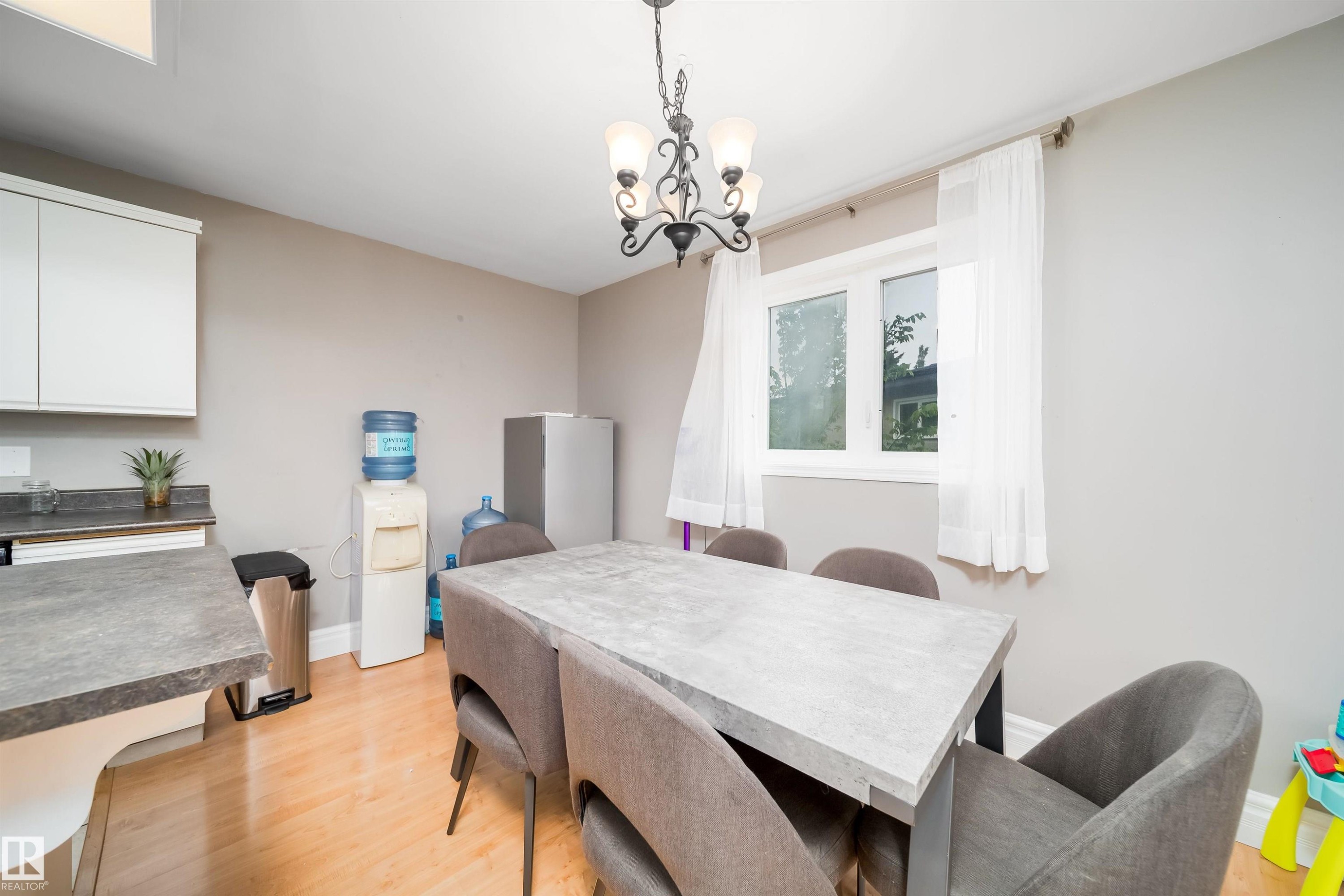 Dining area featuring a modern light fixture, wood-finish flooring, and a large window - 8512 142A Avenue, Edmonton, AB