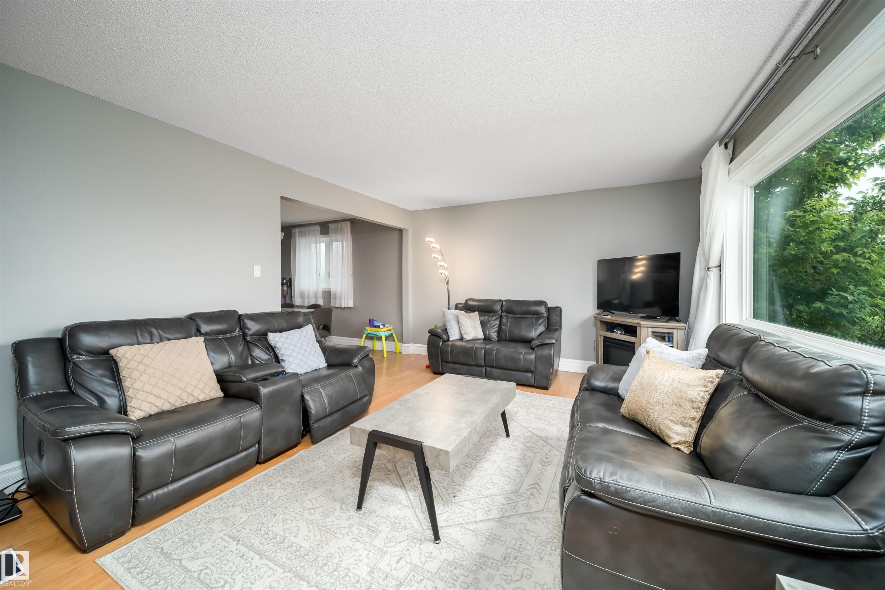 Spacious living area featuring light wood-finish flooring, a large picture window, and a neutral wall palette - 8512 142A Avenue, Edmonton, AB