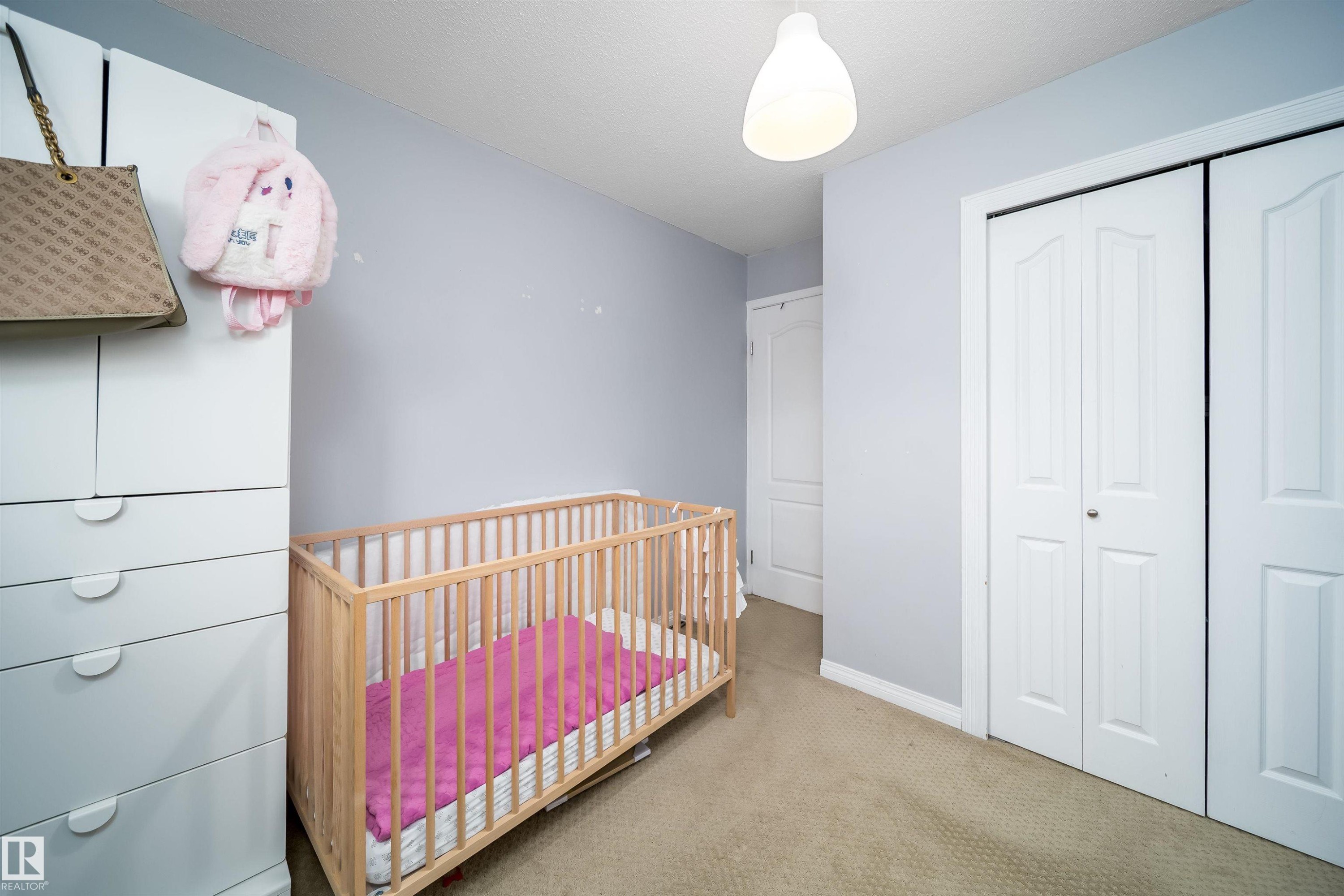 Carpeted room with a ceiling light fixture, bi-fold closet doors, and light-colored walls - 8512 142A Avenue, Edmonton, AB