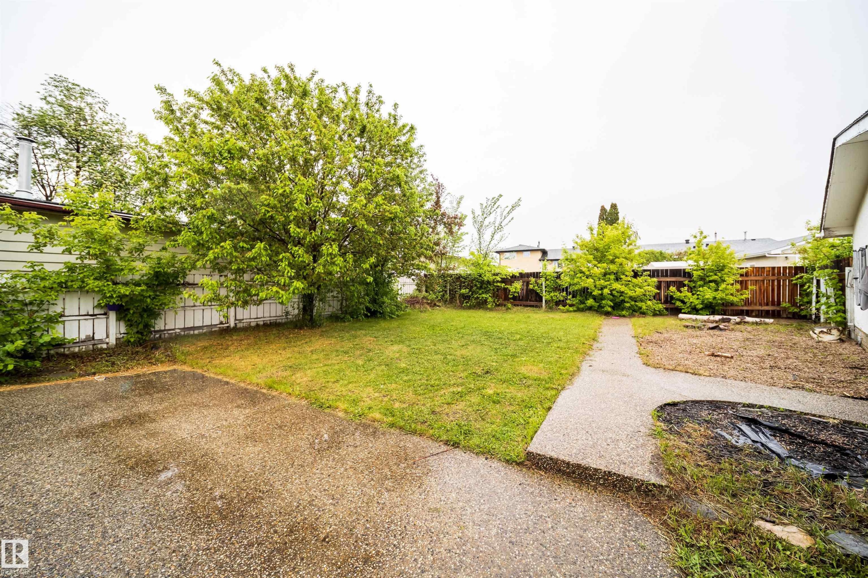 Expansive backyard featuring a large paved patio, a manicured lawn, a concrete pathway, a privacy fence, and mature landscaping - 8512 142A Avenue, Edmonton, AB