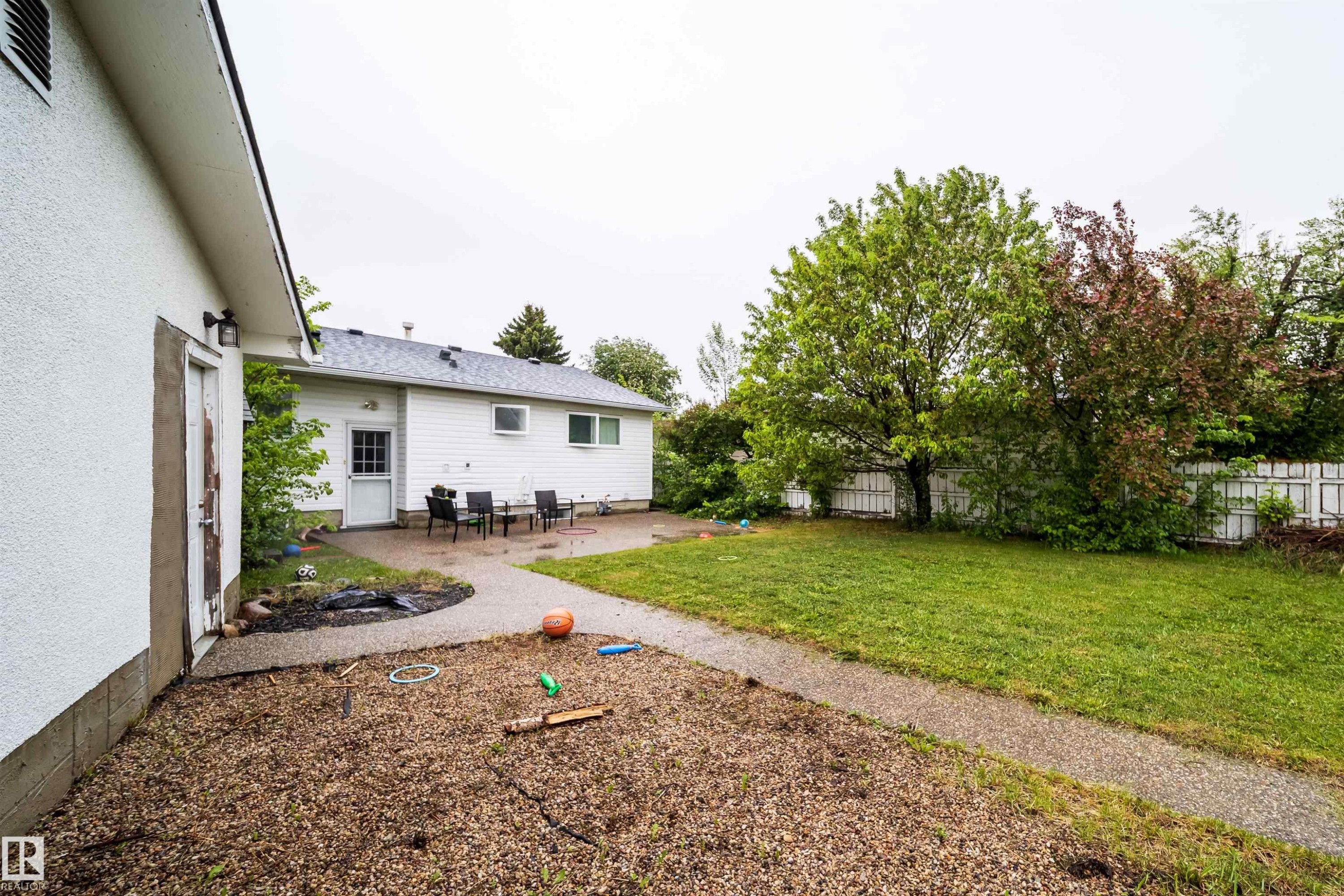 Expansive backyard featuring a large green lawn, mature trees, and a paved patio area - 8512 142A Avenue, Edmonton, AB