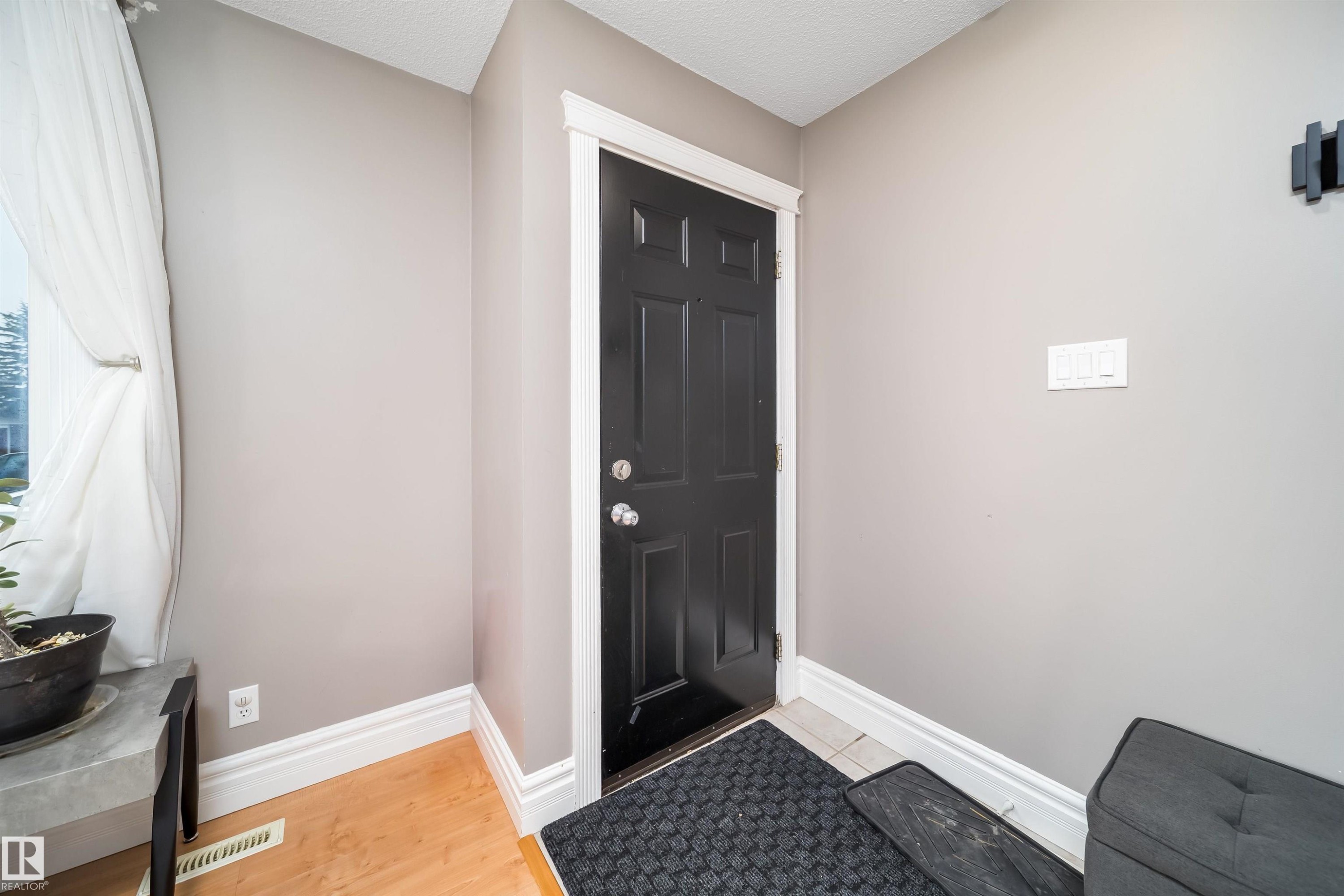 Entryway featuring a paneled black door, light wood-finish flooring, and crisp white trim - 8512 142A Avenue, Edmonton, AB