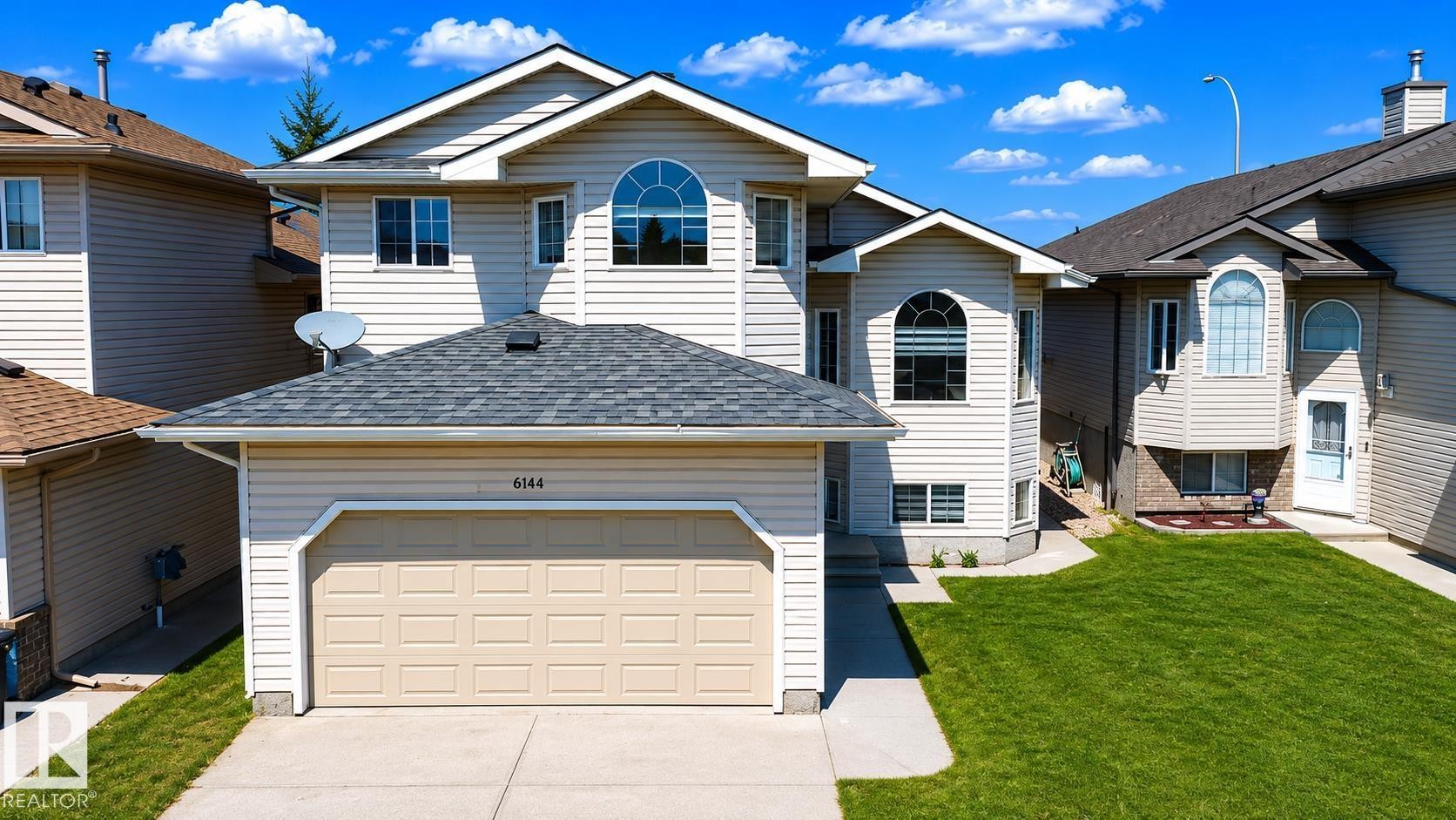 Two-story residence featuring light-colored siding, a prominent attached garage, and arch-top windows - 6144 166 Avenue, Edmonton, AB