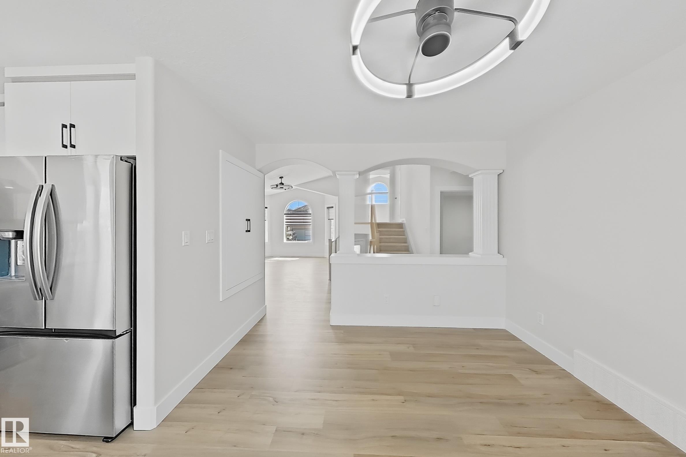 Bright interior space featuring wood-finish flooring, a contemporary ceiling light fixture, white cabinetry, and stainless steel appliances - 6144 166 Avenue, Edmonton, AB