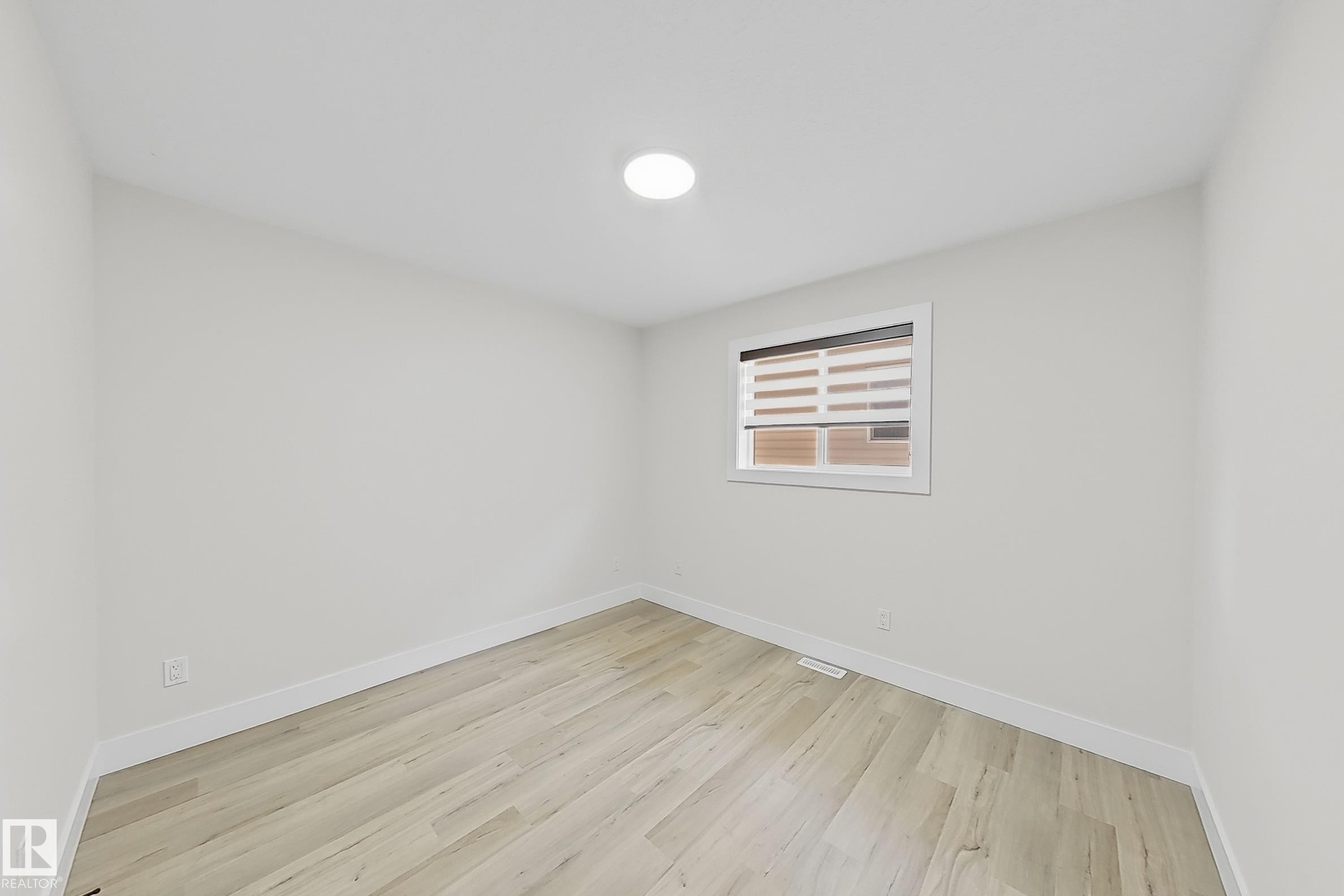 Bright room featuring light wood-finish flooring, white baseboards, and a single window with horizontal blinds - 6144 166 Avenue, Edmonton, AB