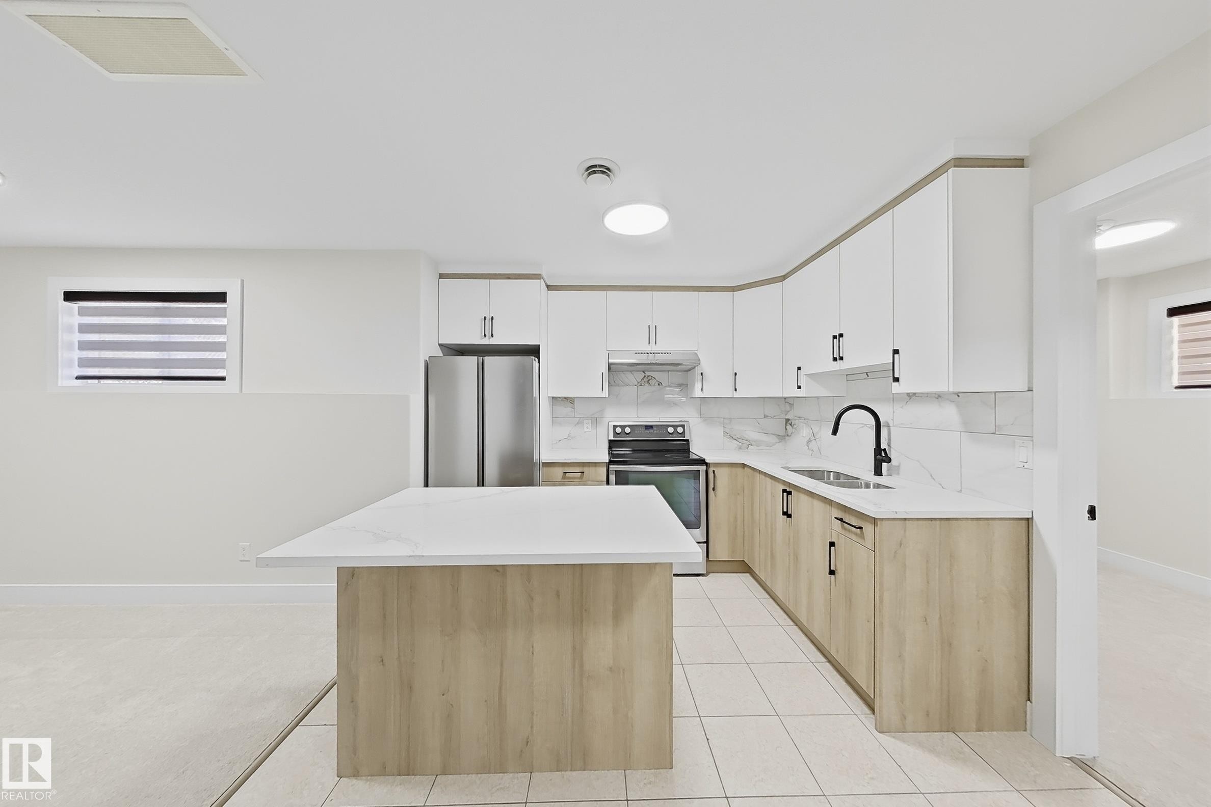 Kitchen featuring a central island with countertop seating, two-tone cabinetry, stainless steel appliances, and a tile backsplash - 6144 166 Avenue, Edmonton, AB