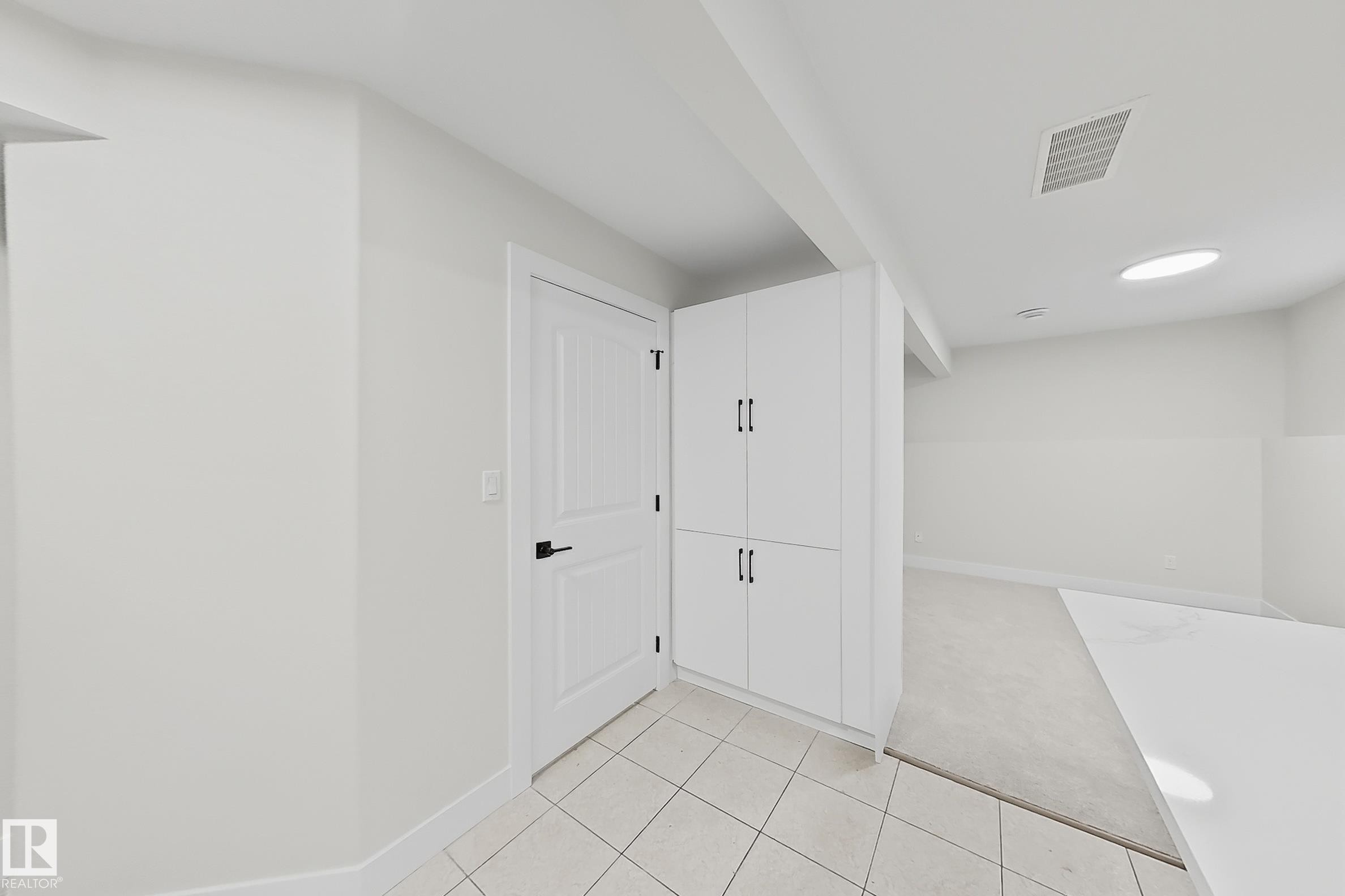 Built-in white cabinetry with black hardware, white paneled interior door, tiled flooring, and a round ceiling light fixture - 6144 166 Avenue, Edmonton, AB