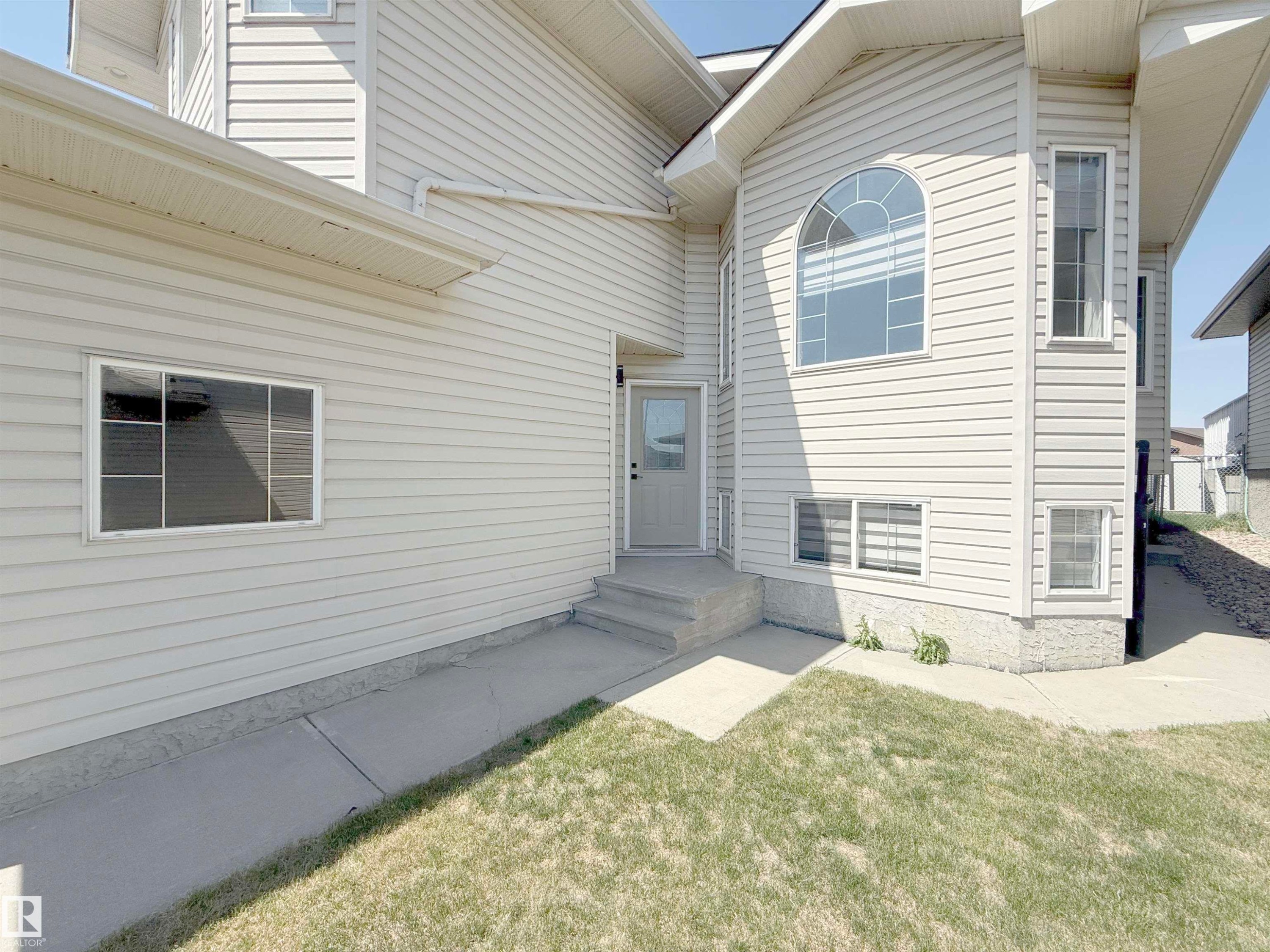 Exterior featuring light-colored horizontal siding, a prominent arched window, multiple rectangular windows, a neutral-toned entry door, and concrete pathways - 6144 166 Avenue, Edmonton, AB