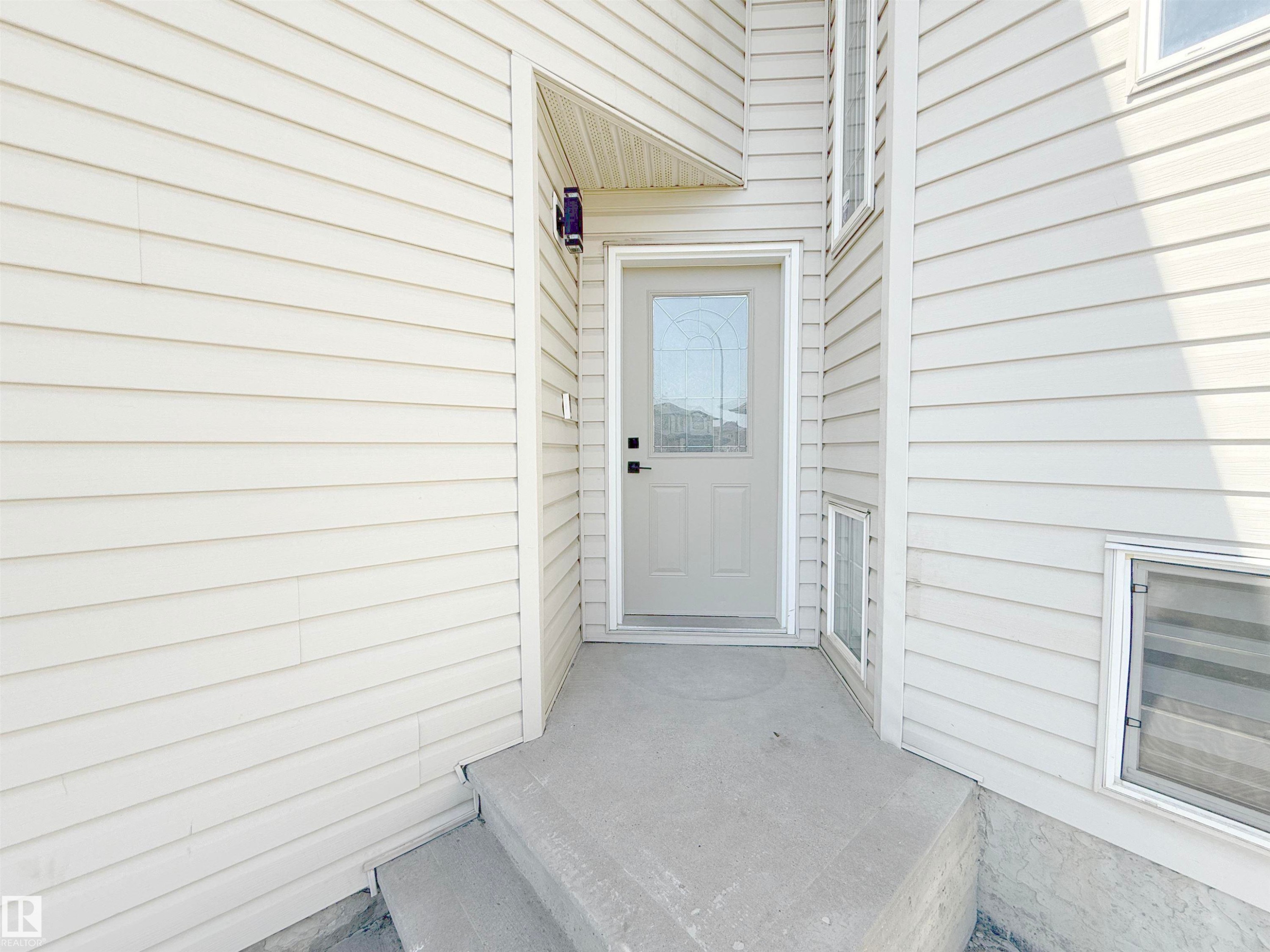 Entryway featuring light-toned horizontal siding, a glass-paneled entry door, and a concrete stoop - 6144 166 Avenue, Edmonton, AB